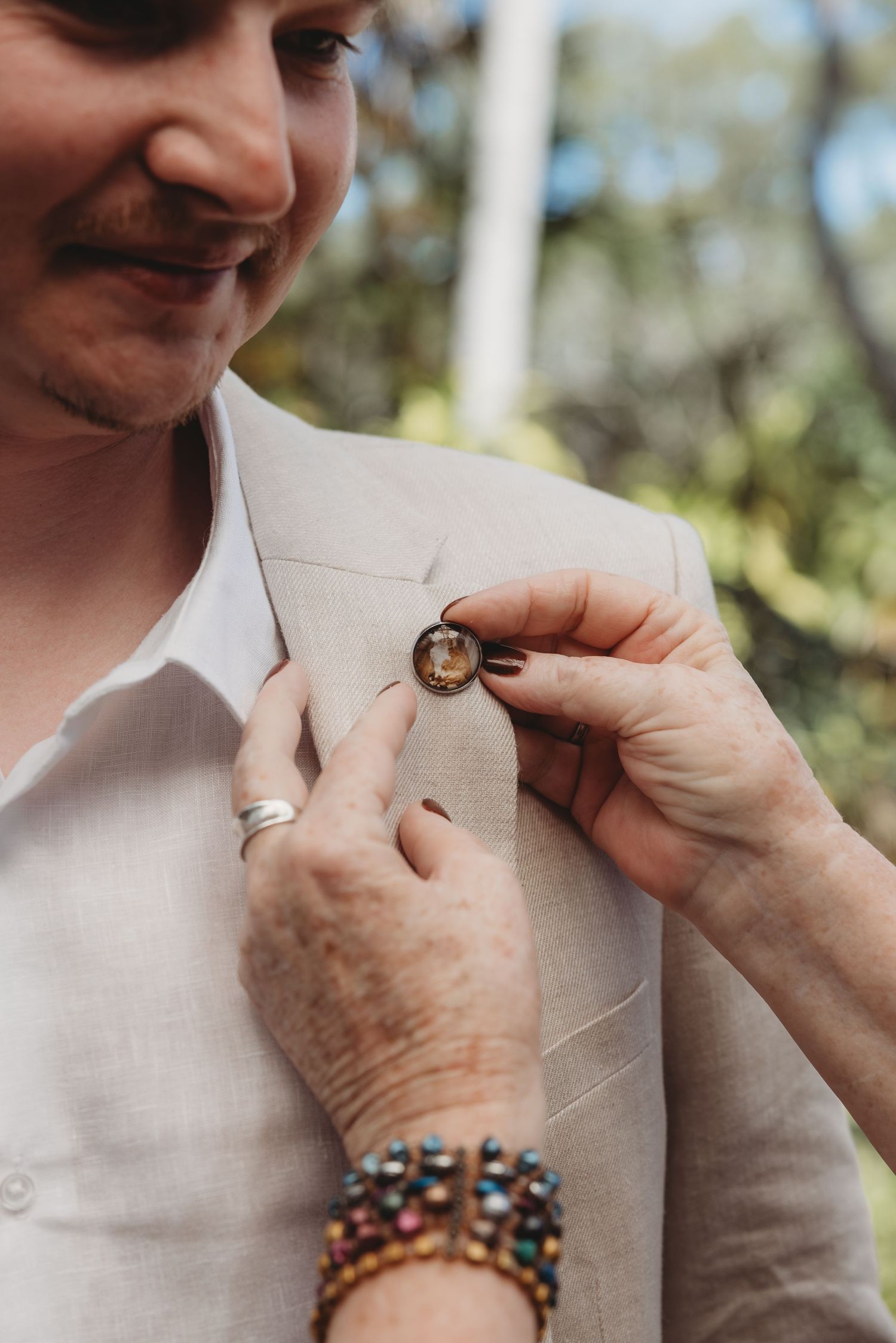 Close-up of hands pinning boutonniere on light beige suit jacket.