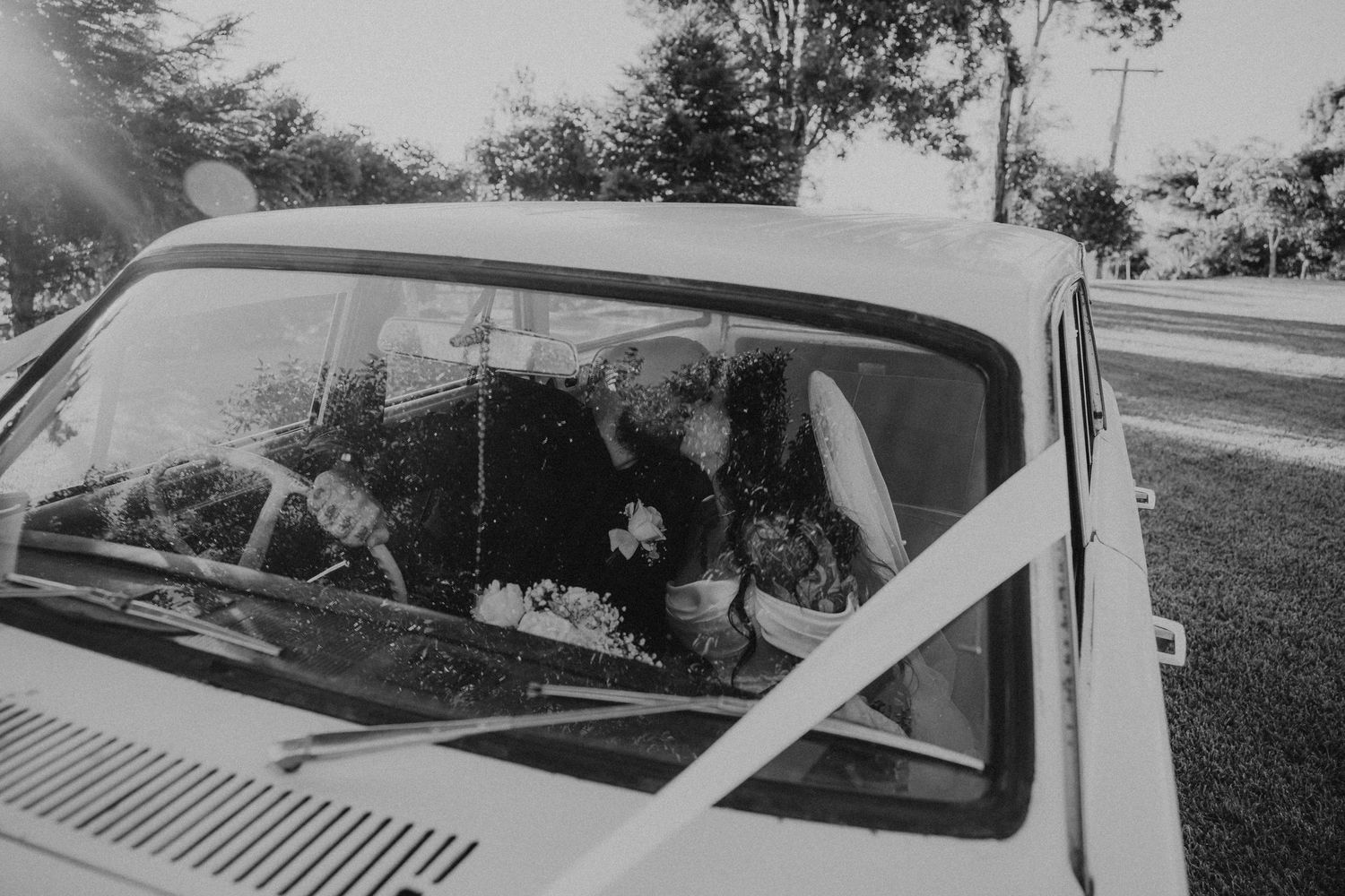 Vintage white car decorated with floral arrangements parked outdoors during a celebration.