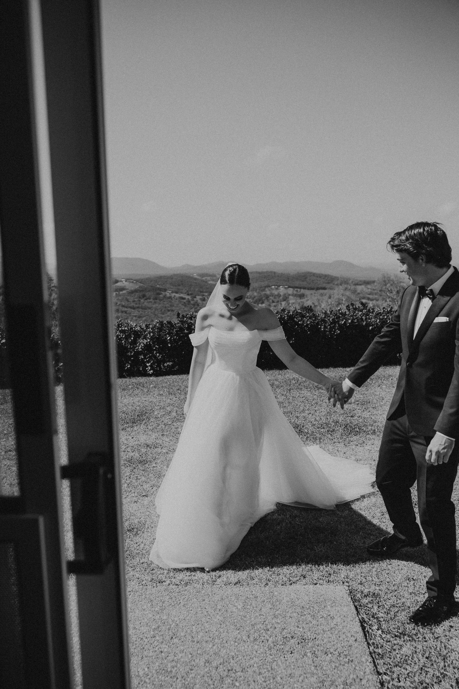 Black and white wedding portrait of couple dancing on a hilltop with mountains in background.