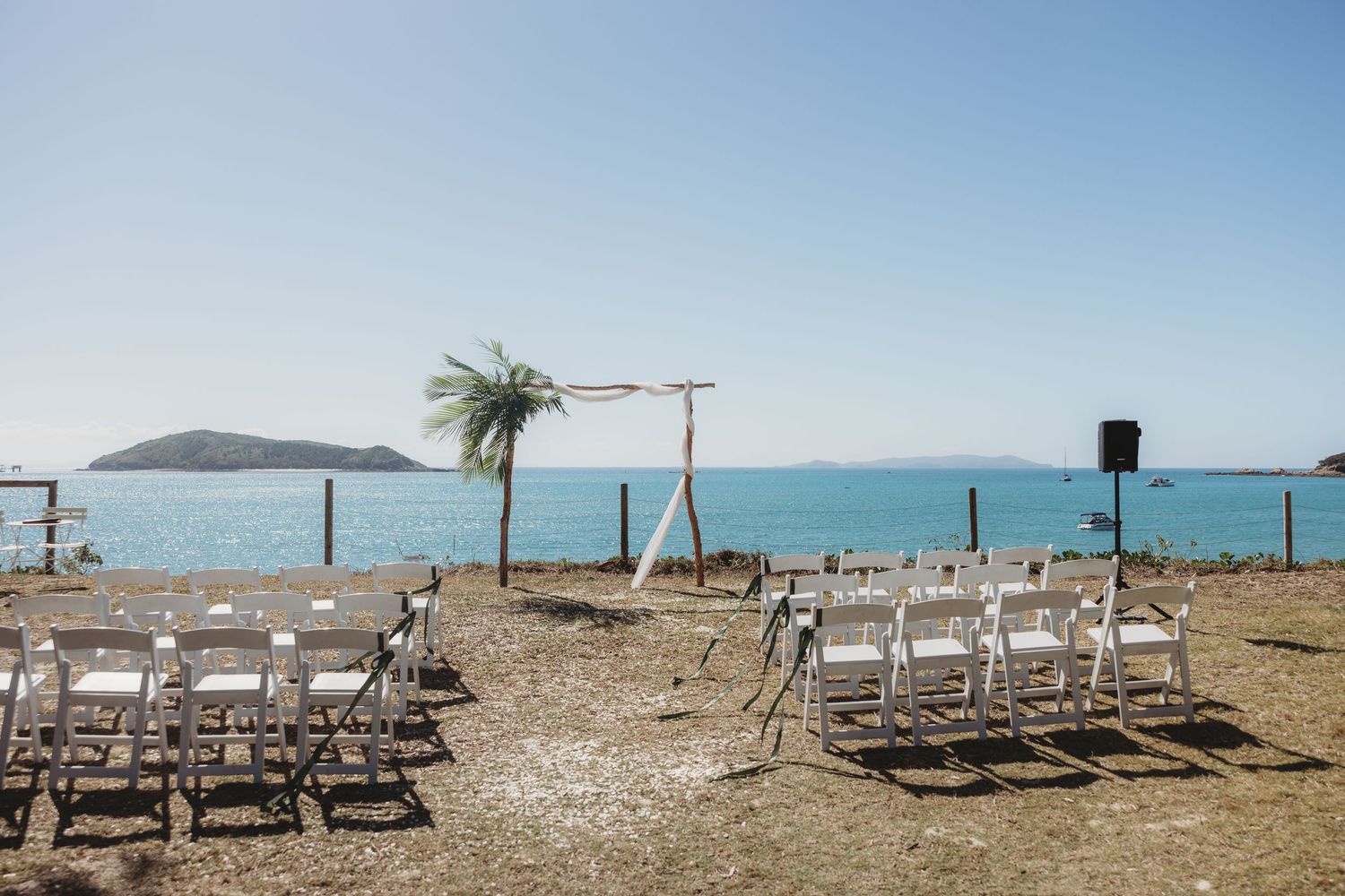 Oceanside wedding ceremony setup with white chairs against blue sky and water.