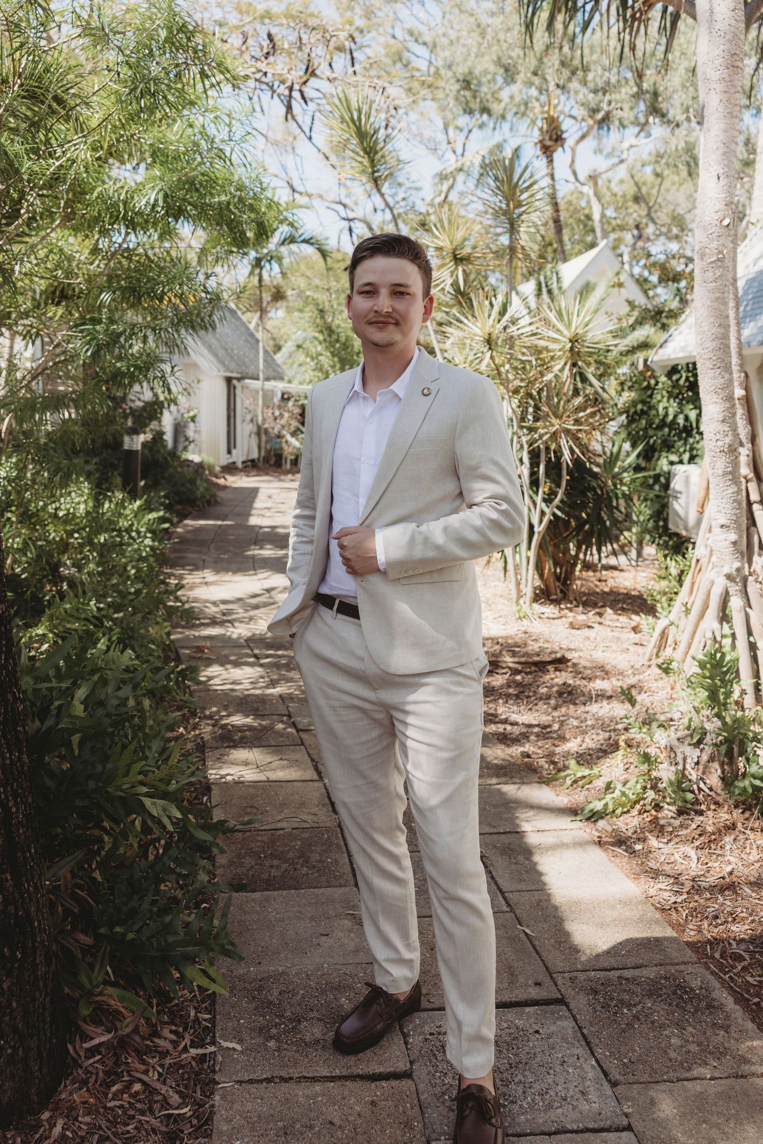 Person in light colored suit poses along a garden pathway with tropical plants.