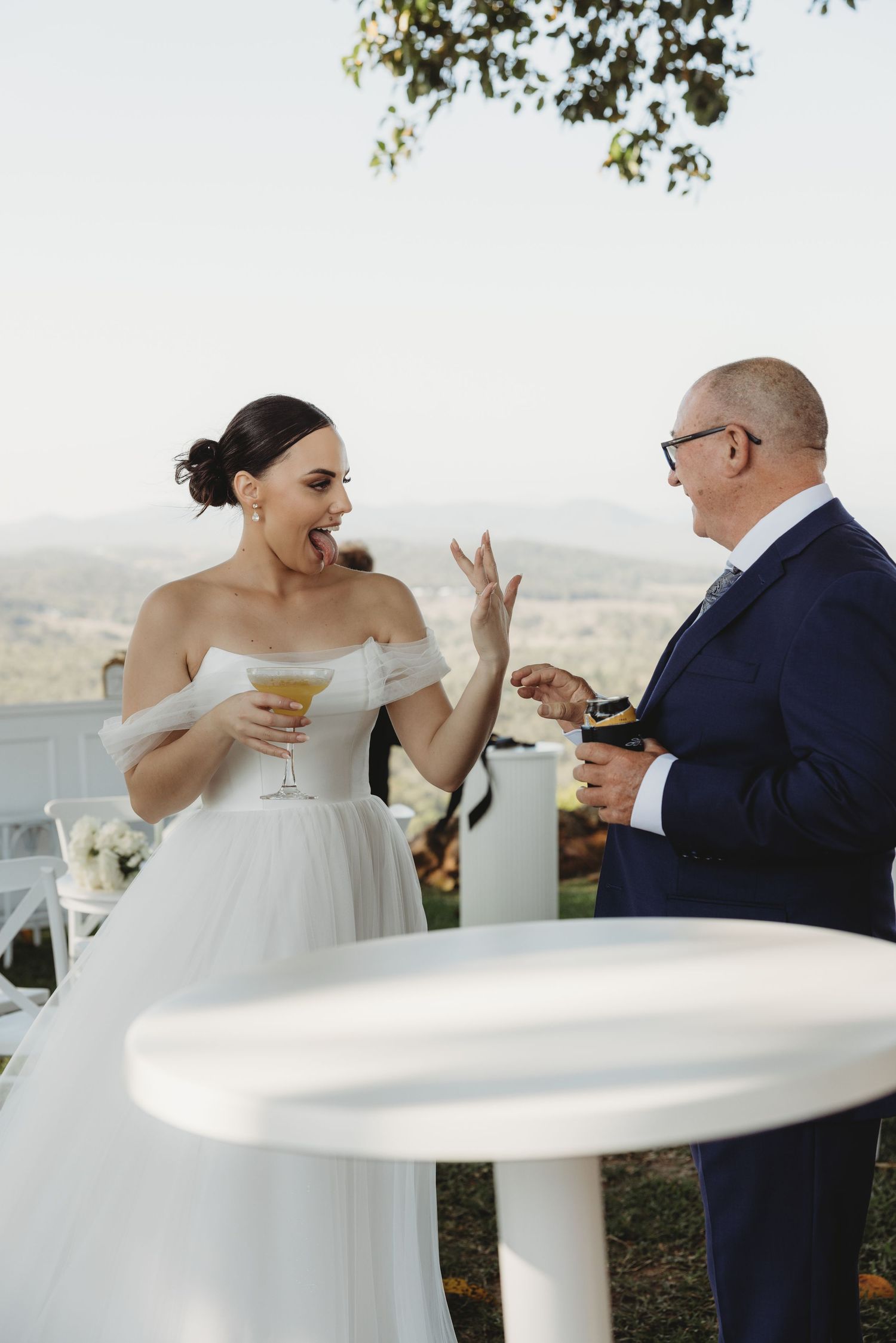 A joyful candid moment between newlyweds sharing drinks at an outdoor wedding reception.