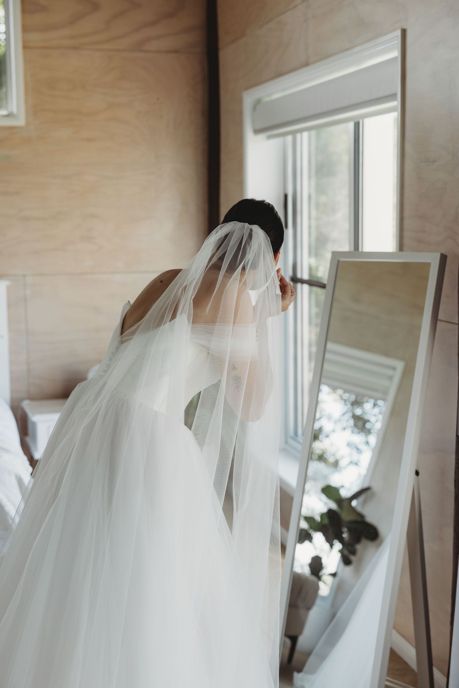 White wedding veil hanging delicately against wooden paneled walls near windows.