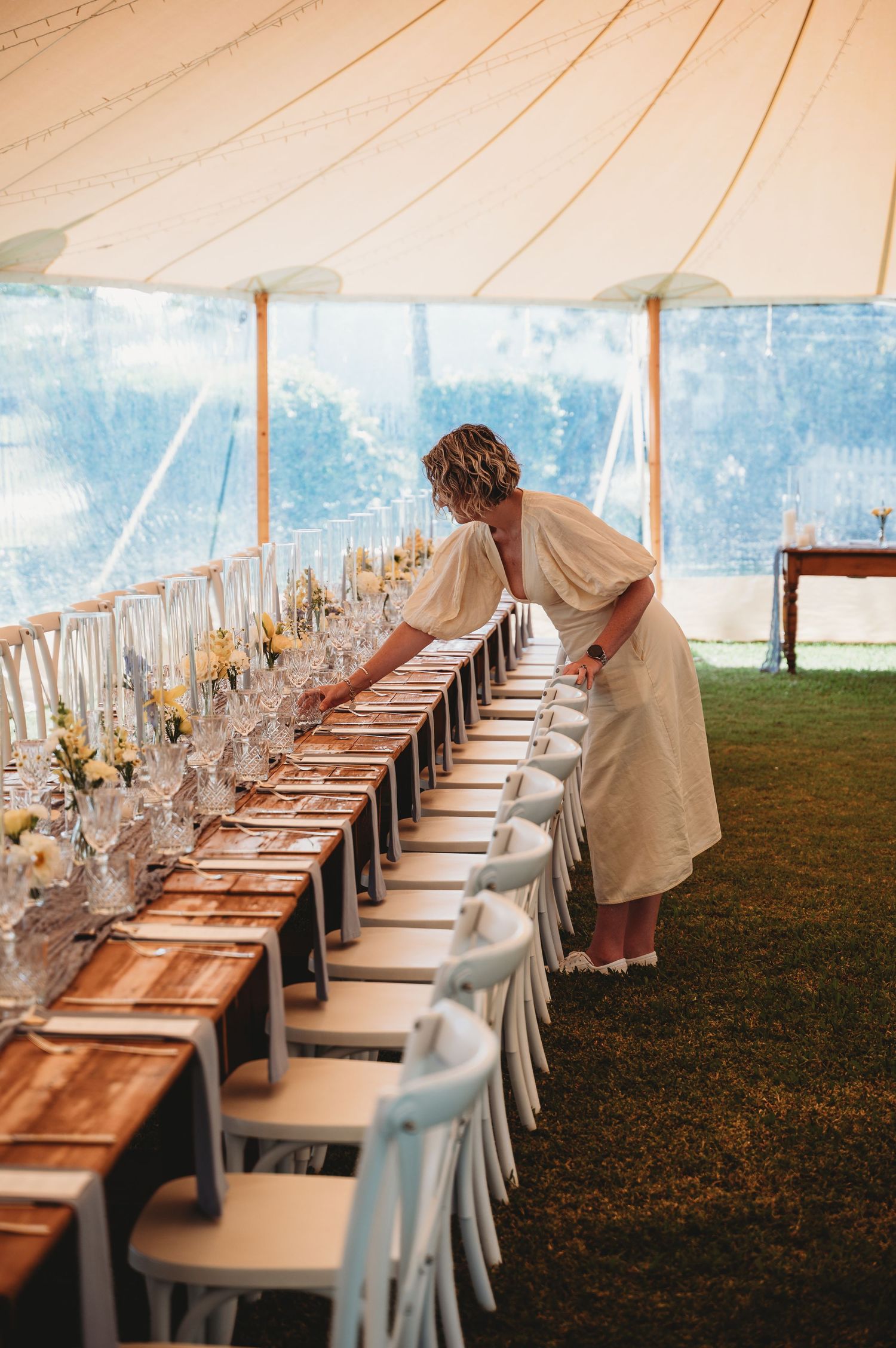 Wedding reception tent with elegant table settings and wooden farm tables arranged in long rows. Lilly & Lotus Rockhampton Weddings stylist