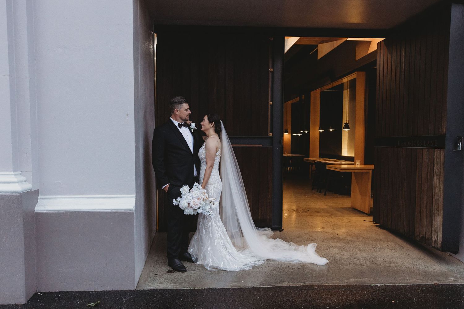 Wedding couple and party pose in a dimly lit indoor venue with modern architecture.