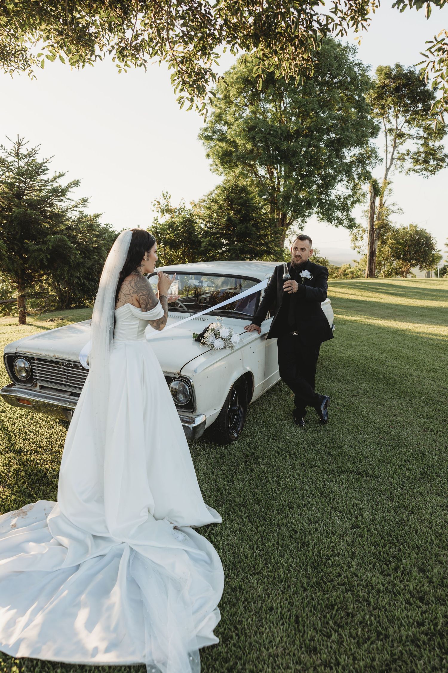 Wedding photoshoot with vintage white car on grassy hill featuring flowing white dress.