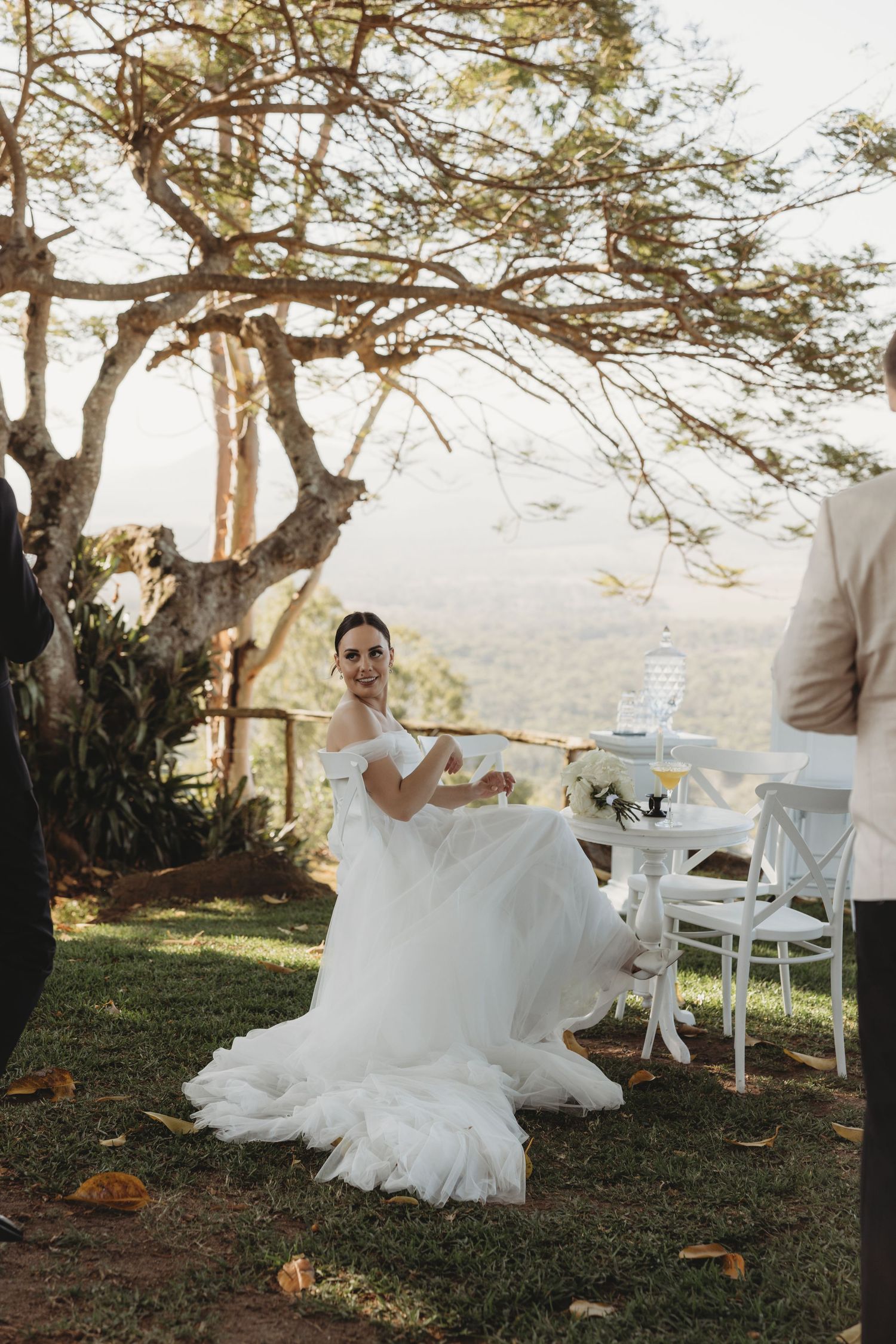 Outdoor wedding setup with white chairs arranged under a scenic tree.