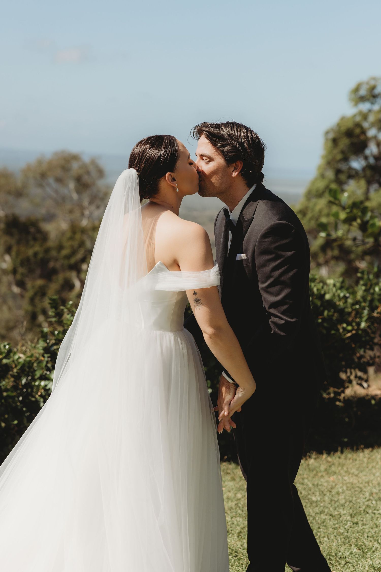A tender kiss between newlyweds during their outdoor wedding ceremony.