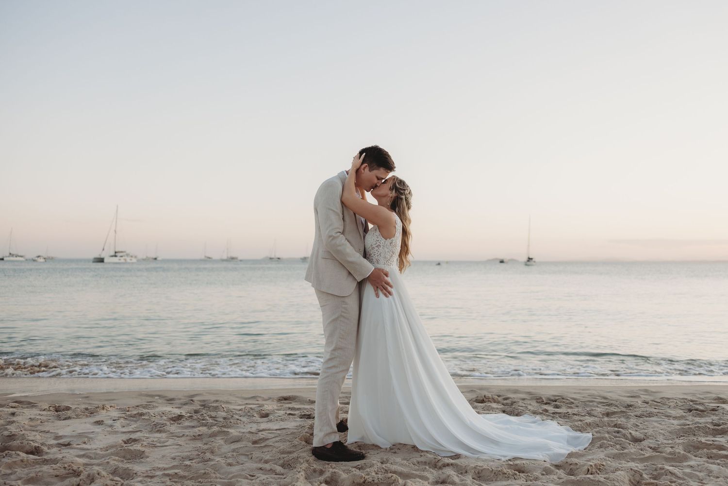 A romantic beachside moment captured during sunset with boats visible in the distance.