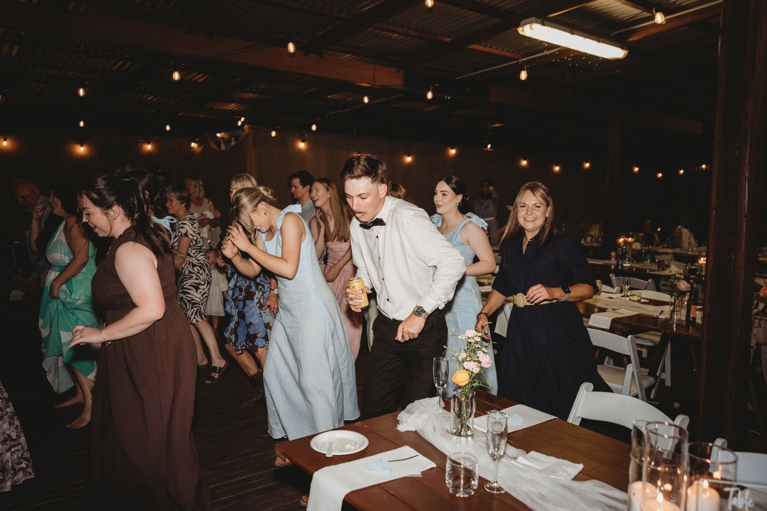 Reception guests gather in a dimly lit venue with tables and decorative lighting.