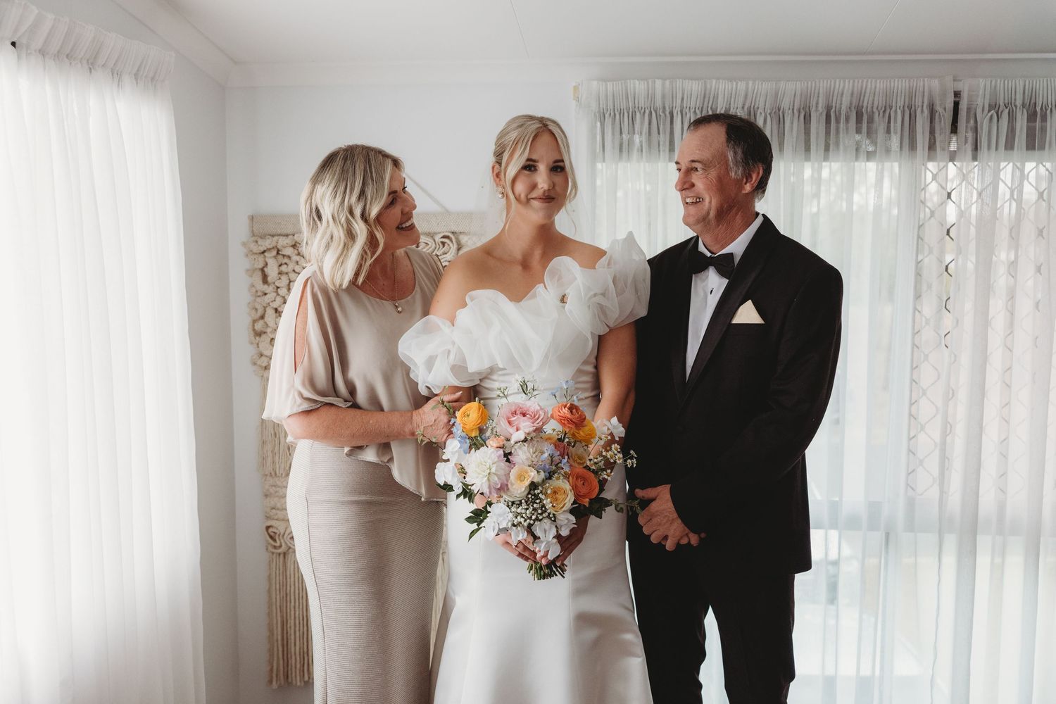 Elegant bridal party poses together in a bright room with white curtains and floral arrangements.