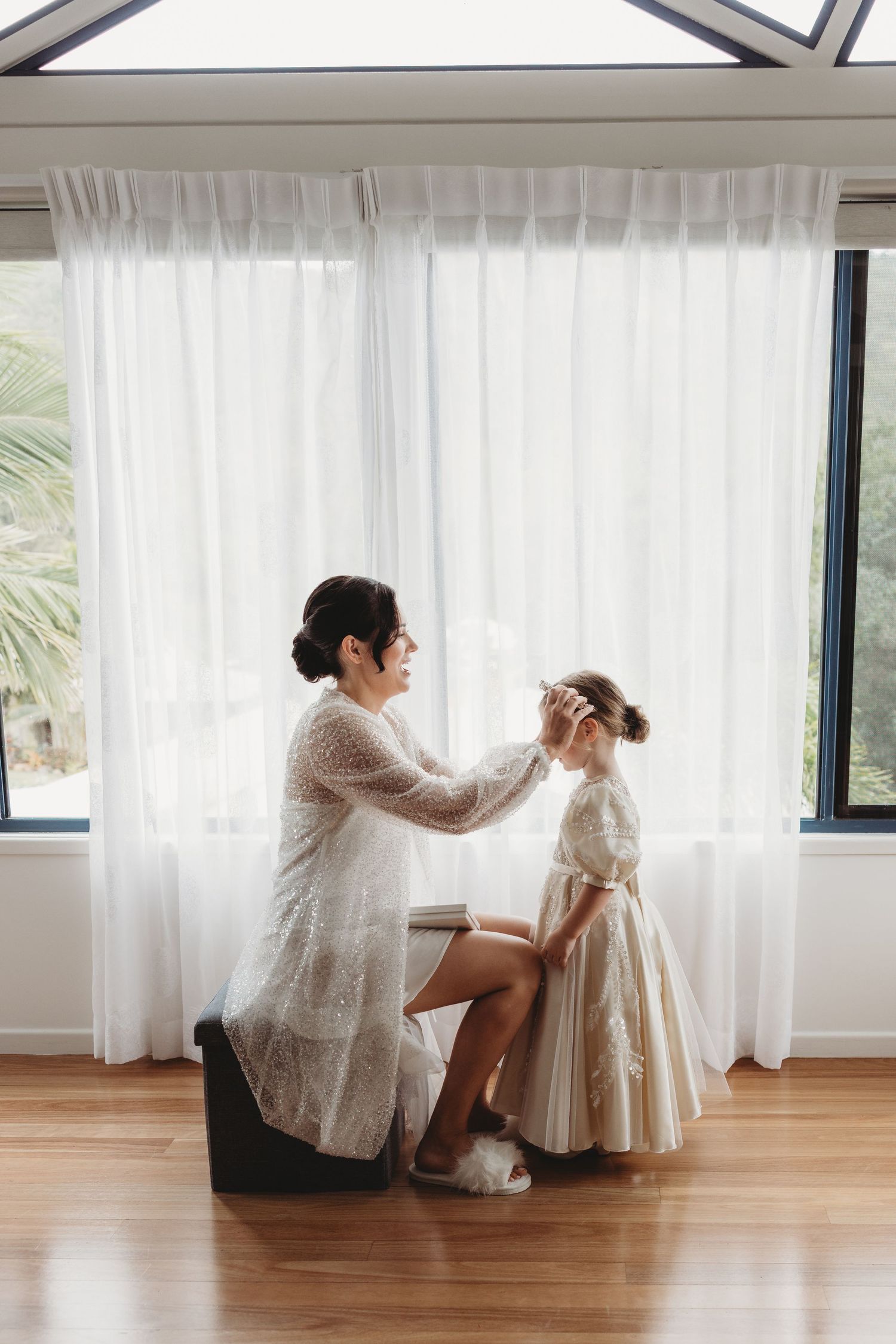 Getting ready scene in bright room with white curtains and hardwood floors.