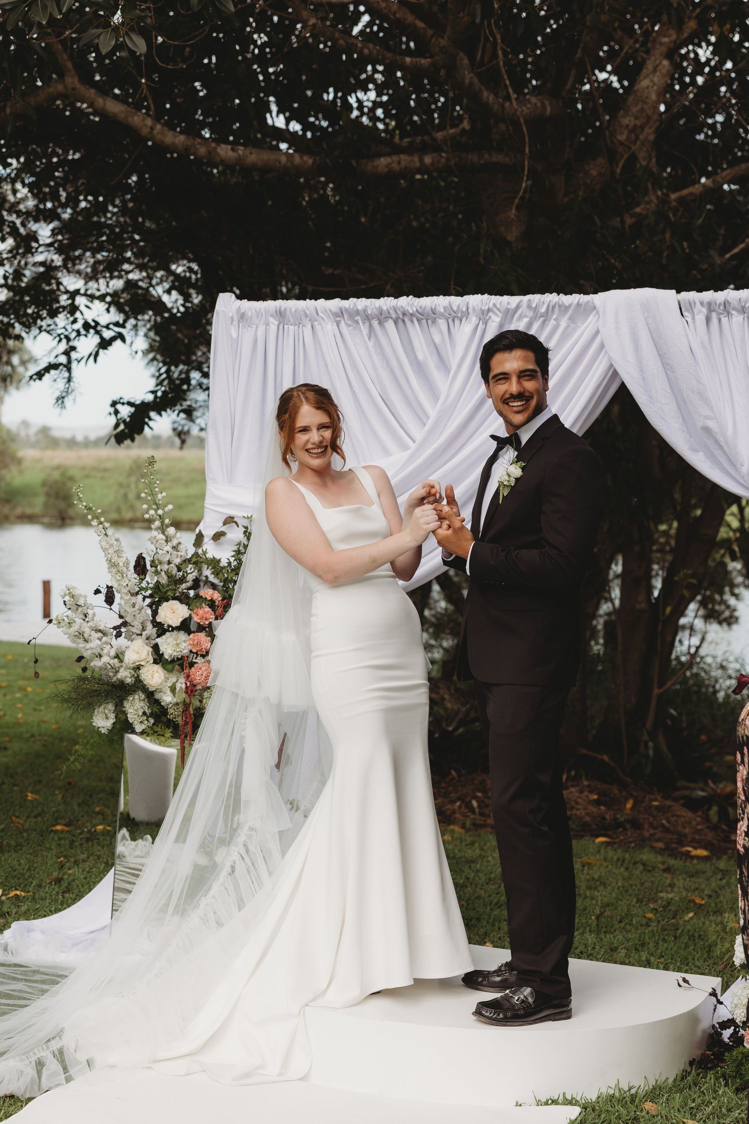 Outdoor wedding ceremony under white draped fabric and floral arrangements.