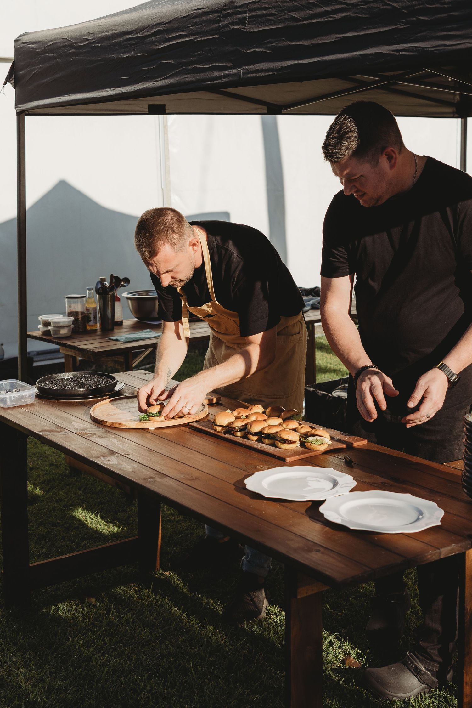 Catering staff preparing food on wooden tables under a white tent at an outdoor event.