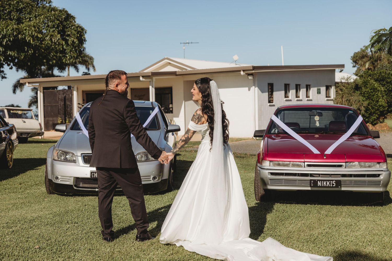 Classic vintage cars line up at an outdoor wedding ceremony on a grassy lawn with white decor.