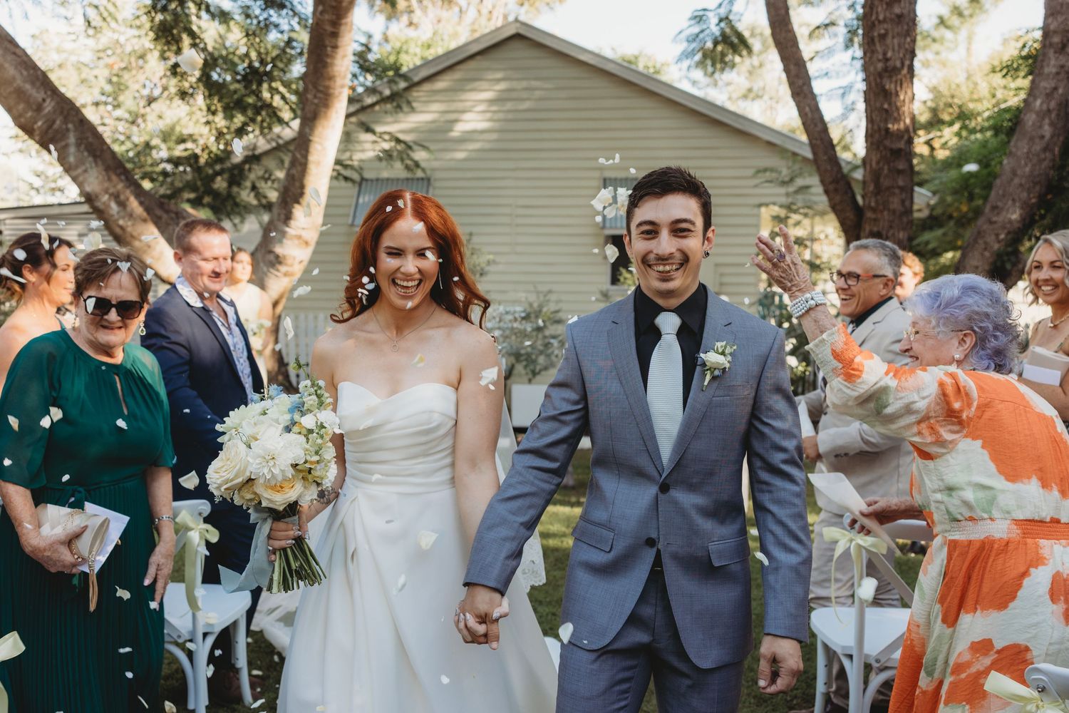Newlyweds walking down the aisle while guests celebrate at outdoor garden ceremony St Aubins Village