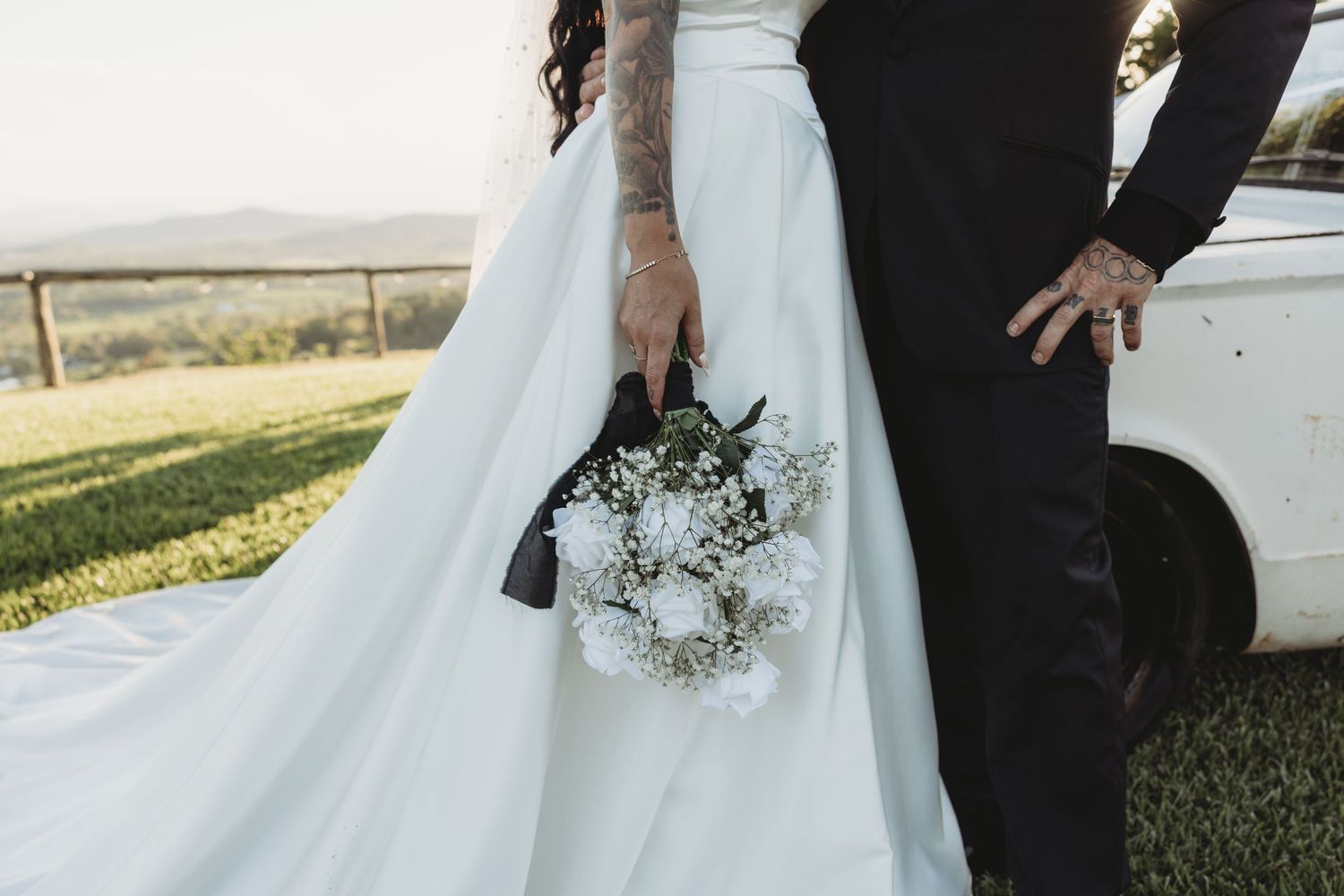 A couple in wedding attire shares intimate moments beside a classic white car.
