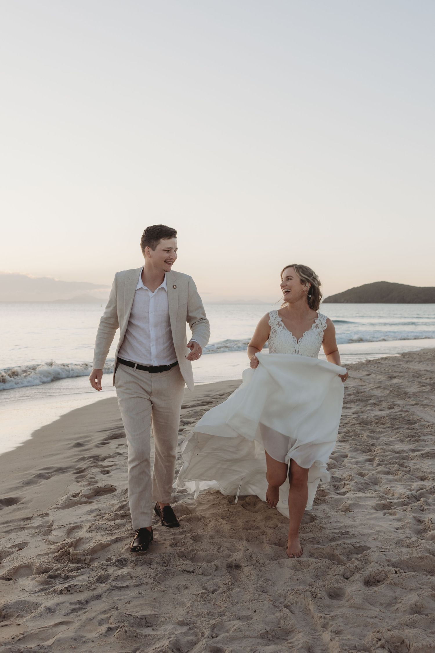 Two people playfully run together on a sandy beach with waves crashing in the background.