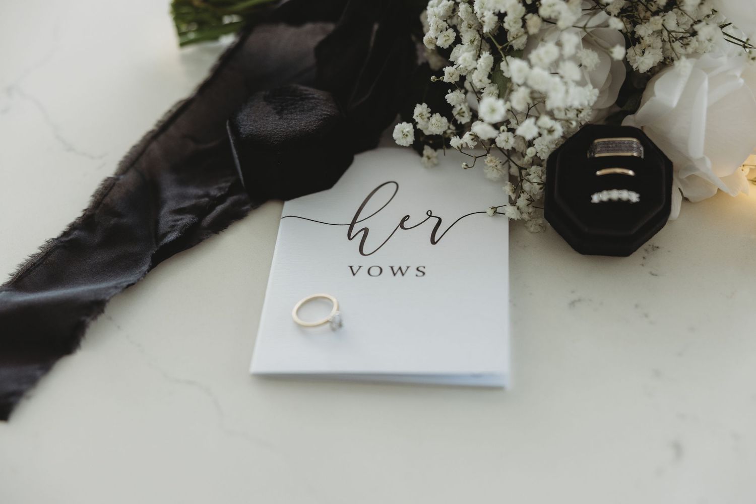 Elegant wedding rings displayed on white surface with delicate floral decor and paper details in soft lighting.