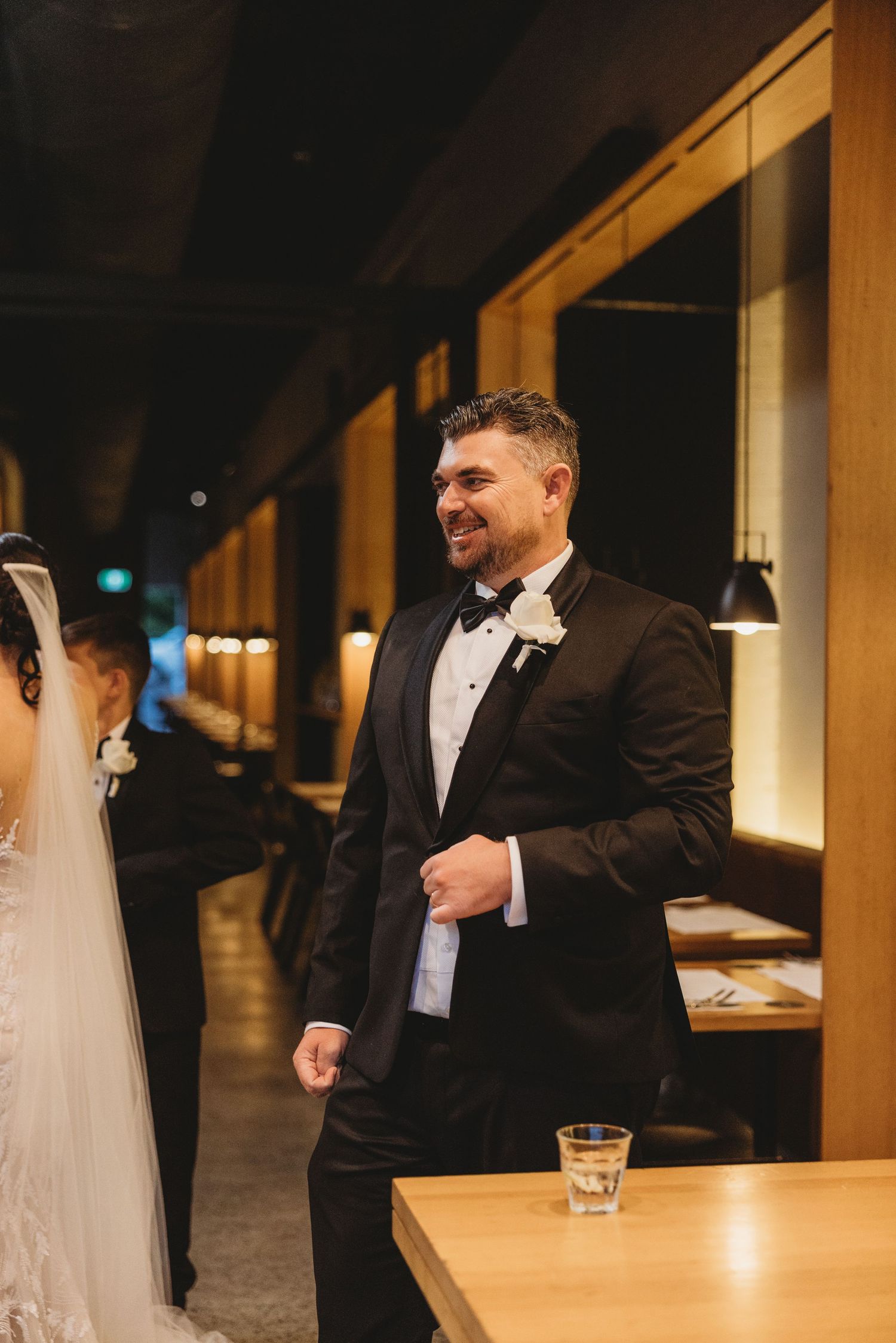 Wedding party members in formal black tuxedos gathered at a dimly lit bar.