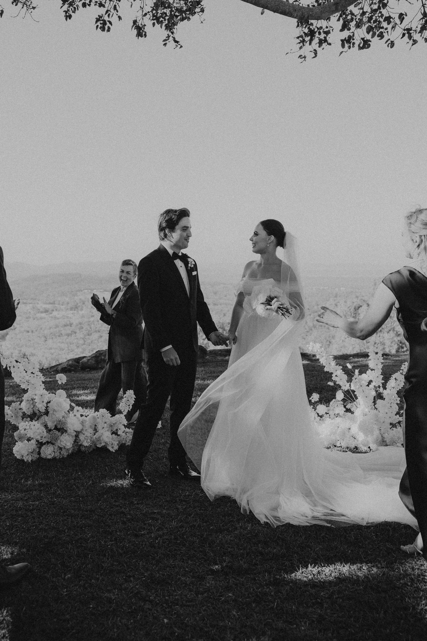 Black and white wedding photos showing playful moments between the couple on a grassy hillside.