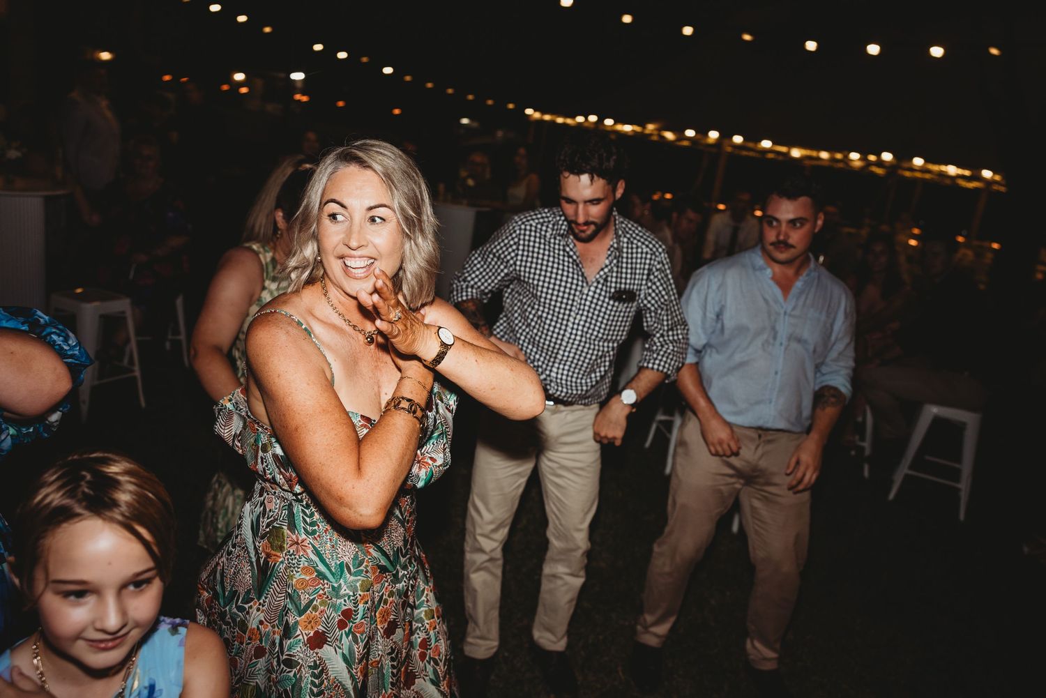 Wedding reception guests dancing and celebrating under string lights at night.