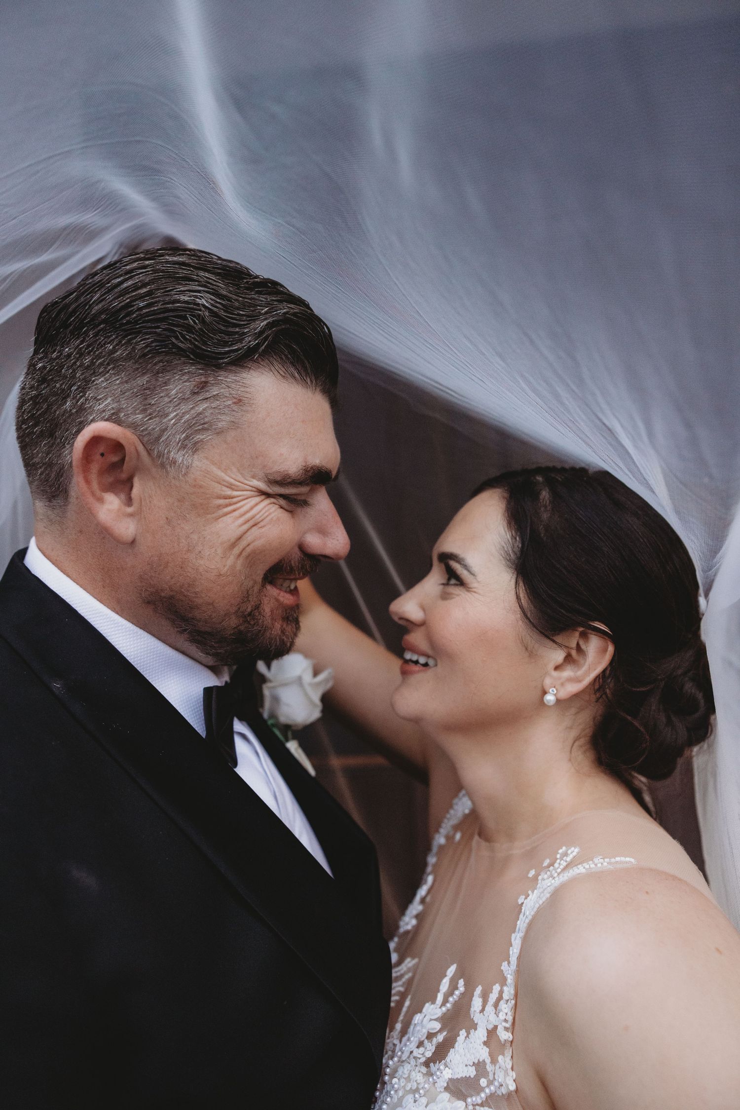 A romantic moment shared under a flowing veil during a formal wedding celebration.