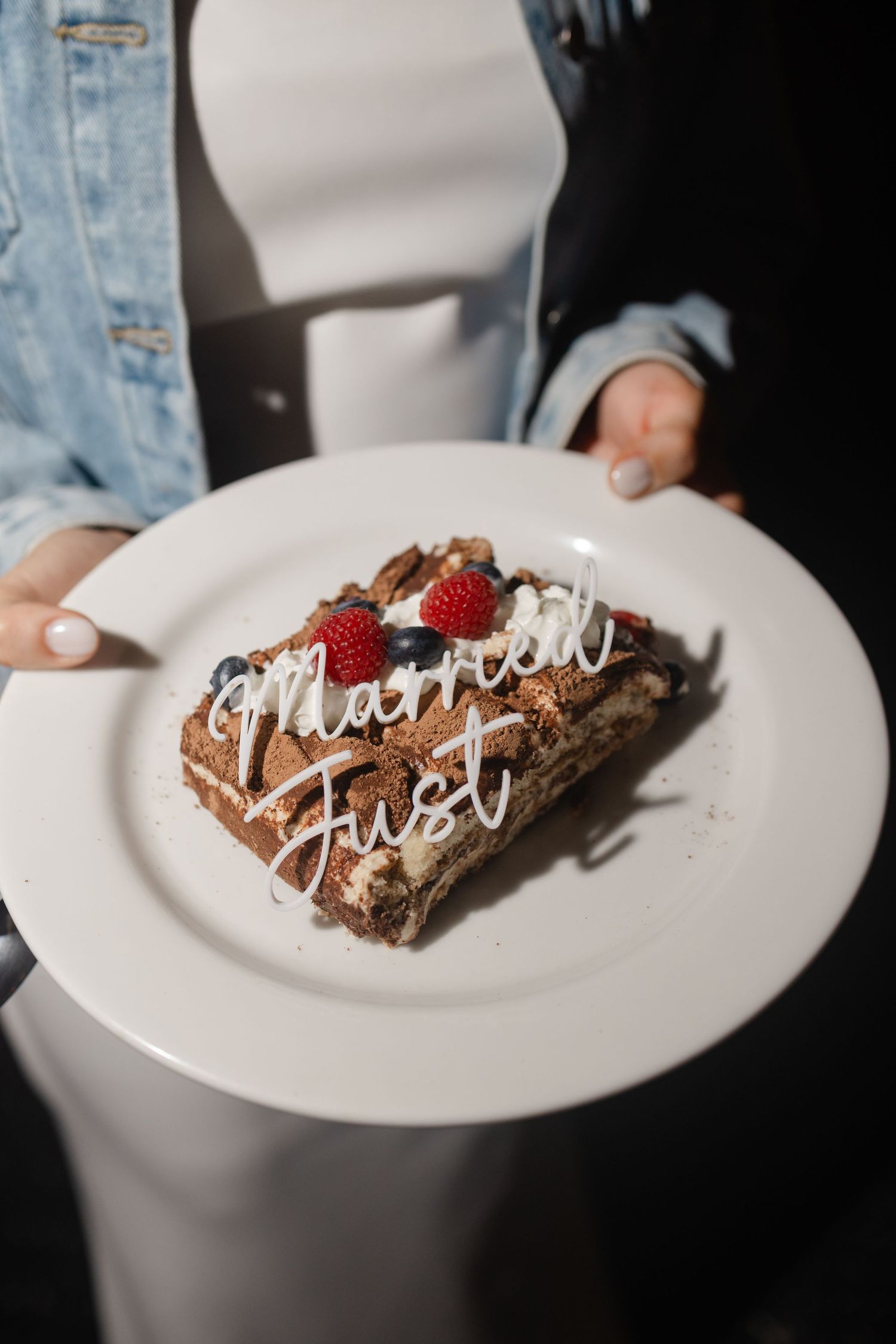Person holding a white plate with a chocolate cake slice topped with berries and 