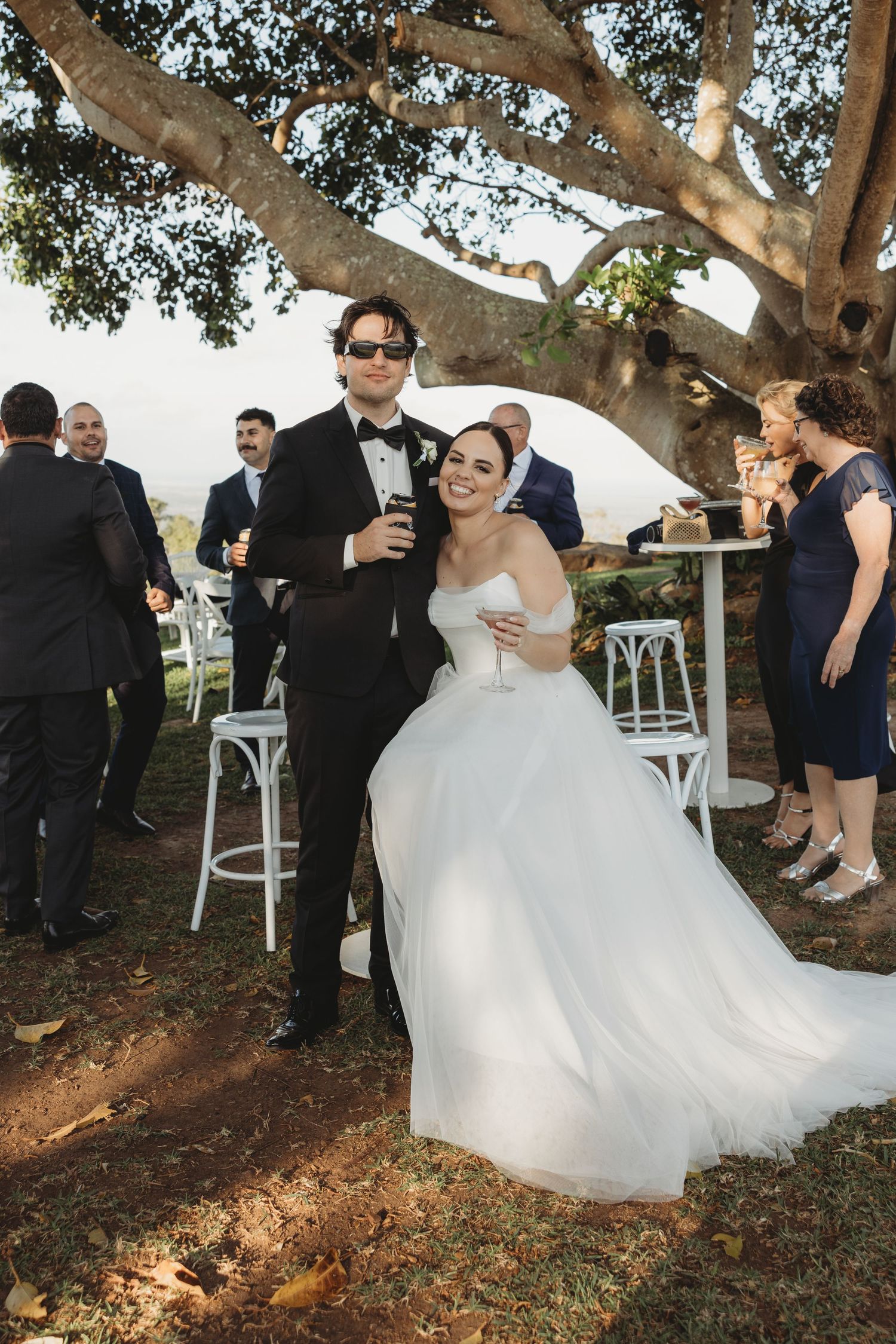 Wedding party celebrates under a majestic tree during an outdoor reception.