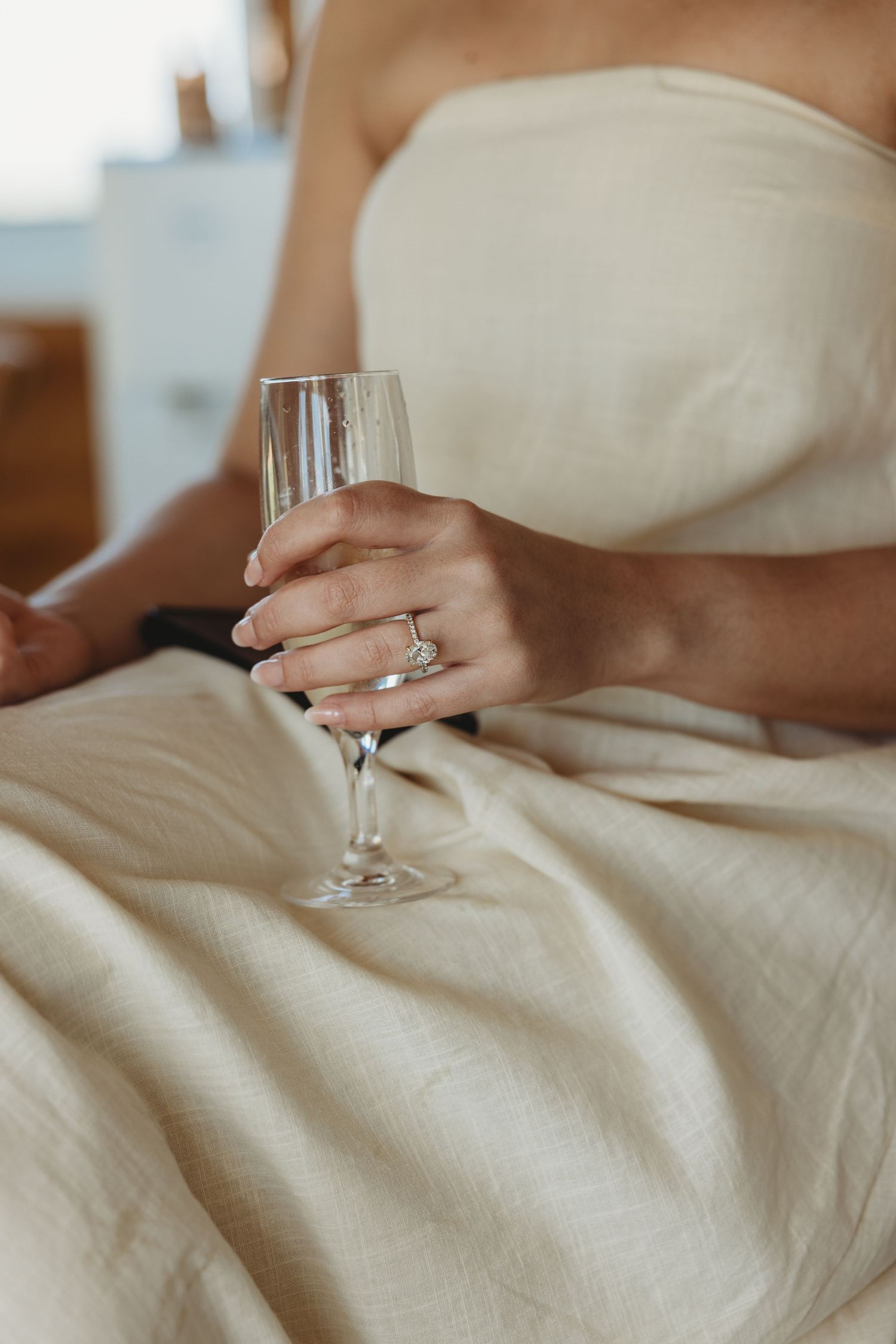 Hands holding a wine glass against white fabric in soft natural lighting.