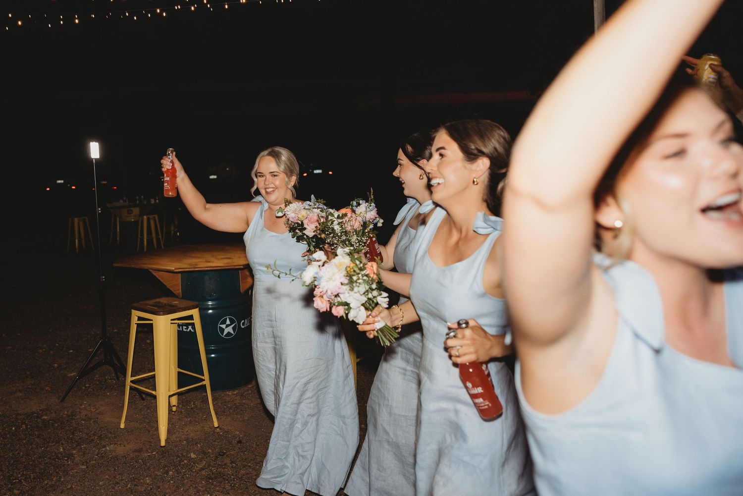 Wedding party dancing and celebrating at an evening reception under string lights.