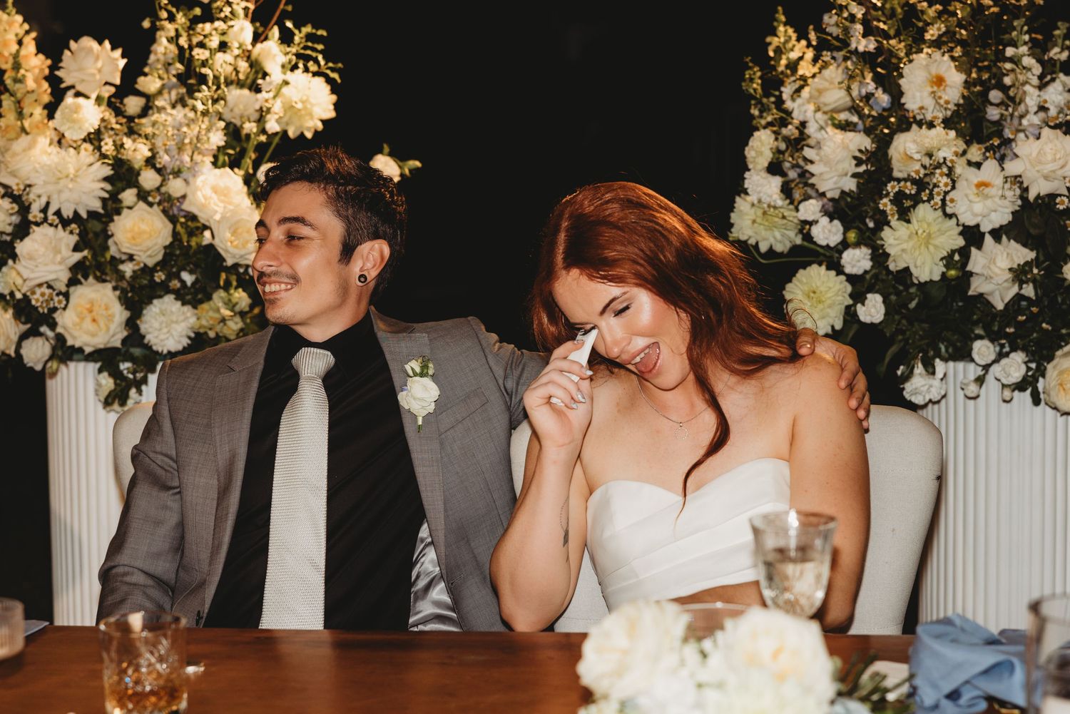 Couple sharing an intimate moment during their wedding reception with floral decor and string lights in the background.