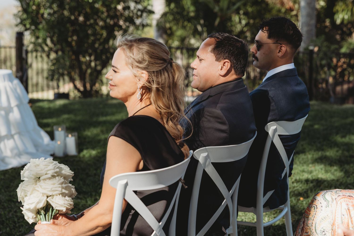 Wedding guests seated in elegant white chairs during an outdoor garden ceremony.