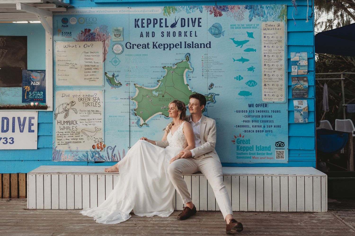 Wedding couple poses against a blue wall with nautical themed signage and decorations.