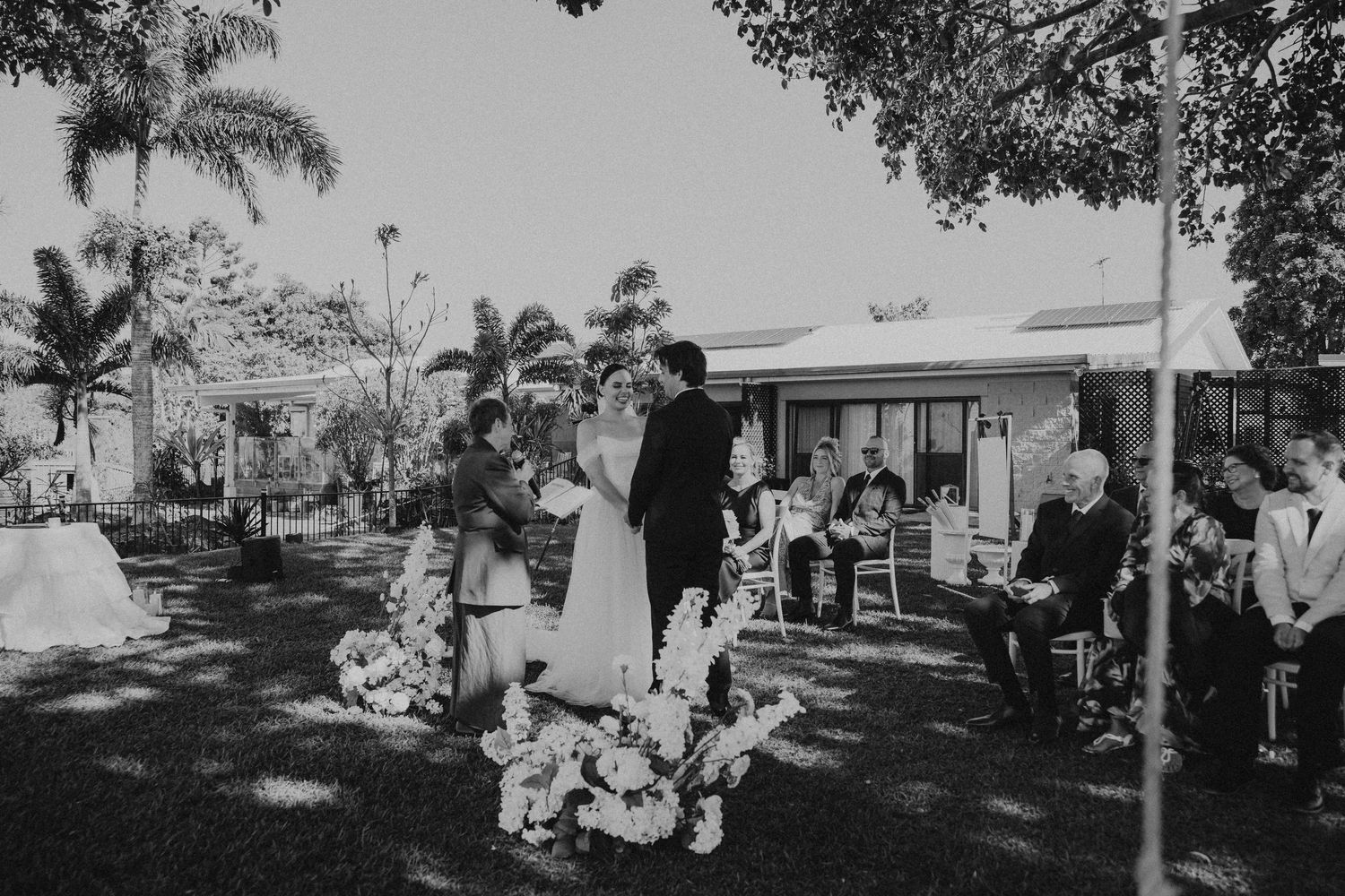 Black and white photo of an outdoor wedding ceremony with palm trees and natural lighting.