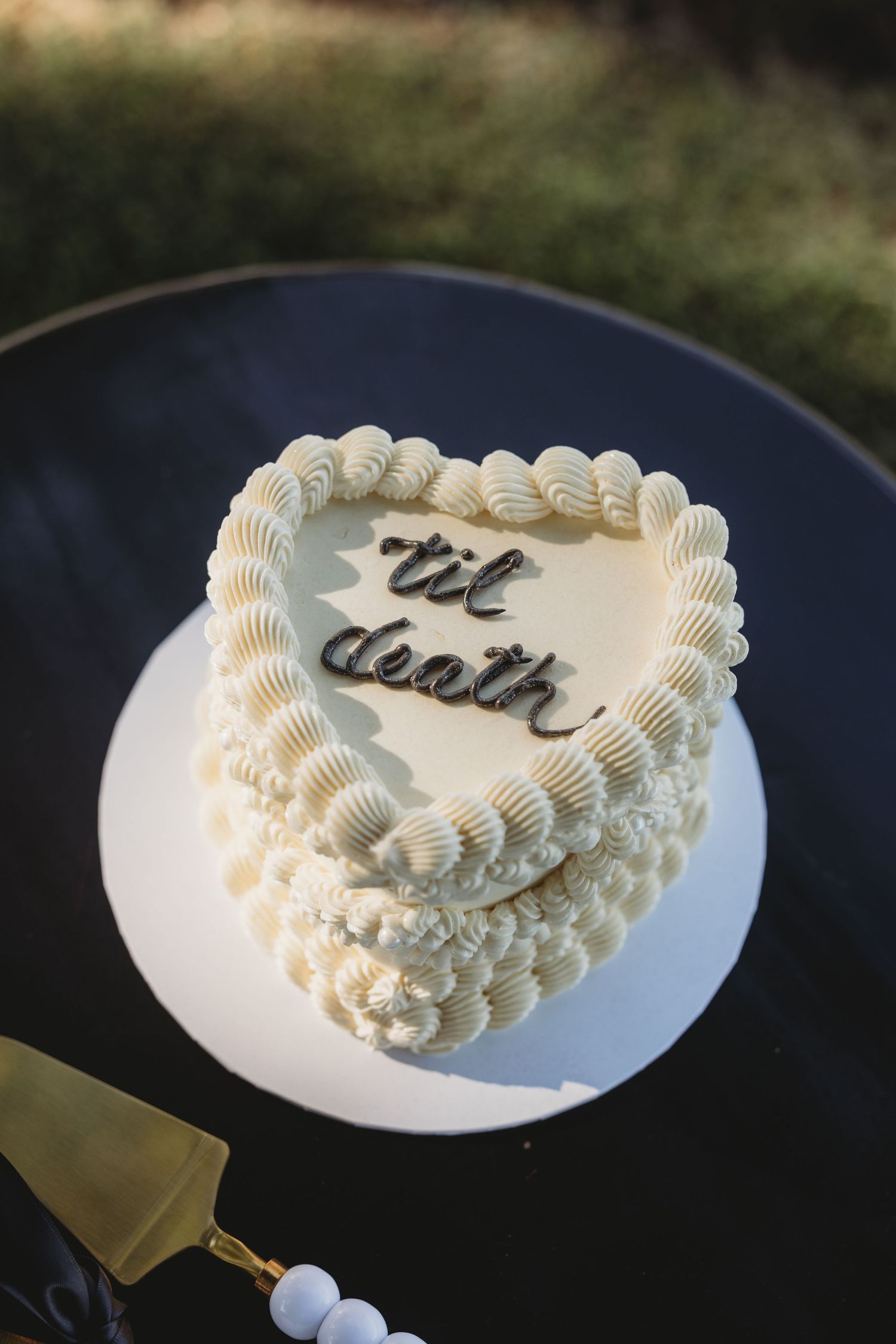 White wedding cake with piped frosting decorations being cut on a dark surface.