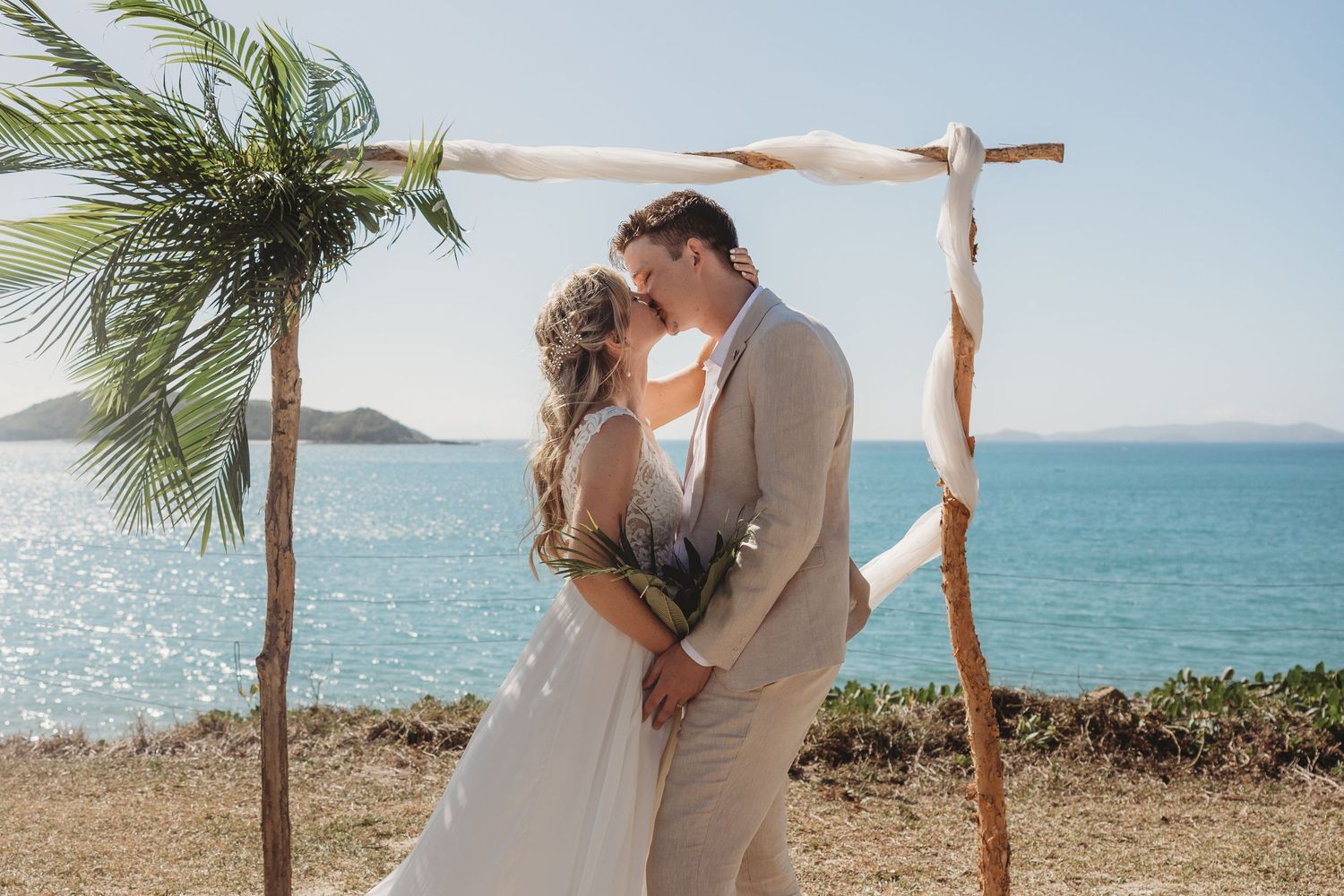 Romantic beach wedding ceremony with palm trees and ocean backdrop.