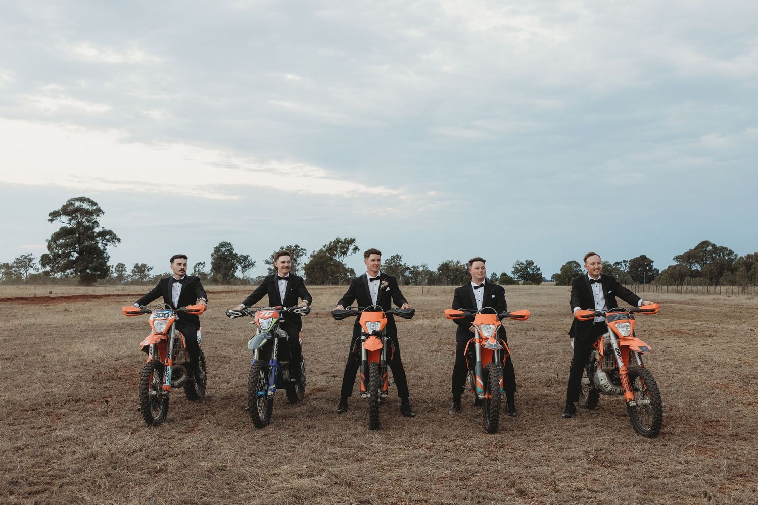 Row of dirt bikes lined up in field during rustic outdoor wedding shoot.