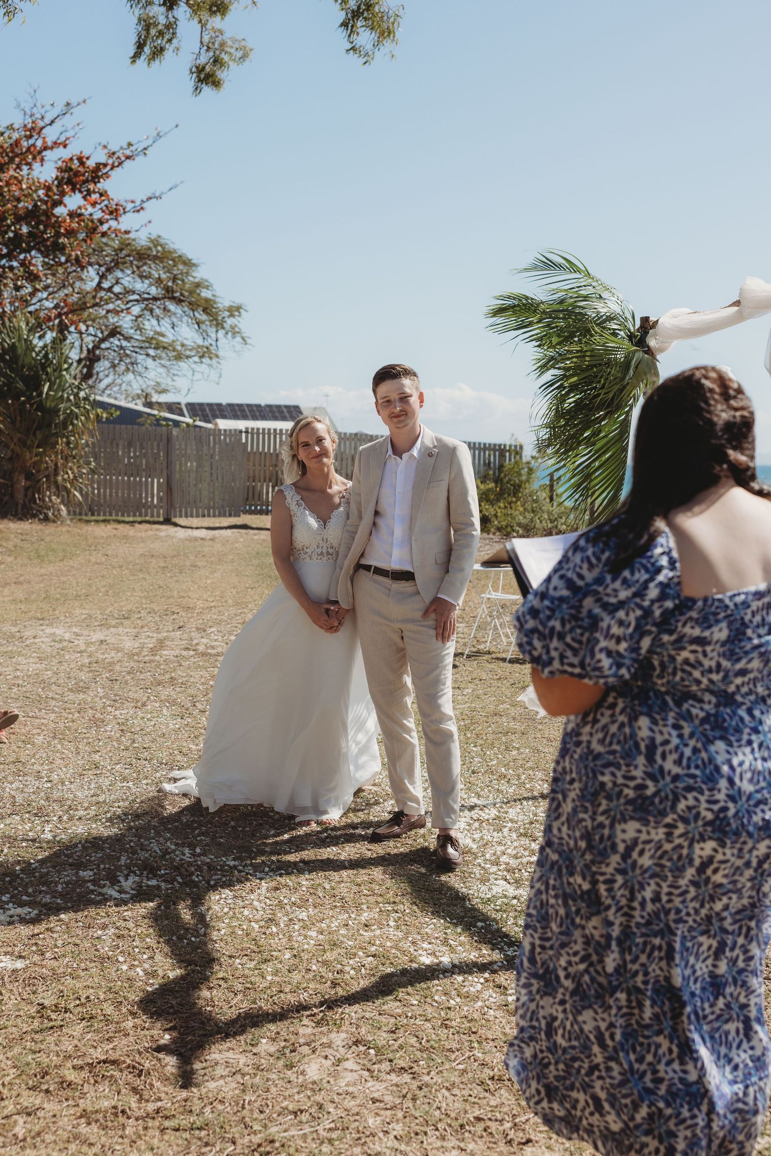 Wedding photographer captures couple and guest in floral dress against natural outdoor backdrop.