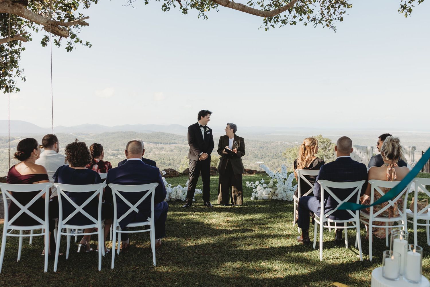 Guests seated in white cross-back chairs watching an outdoor wedding ceremony with mountain views.
