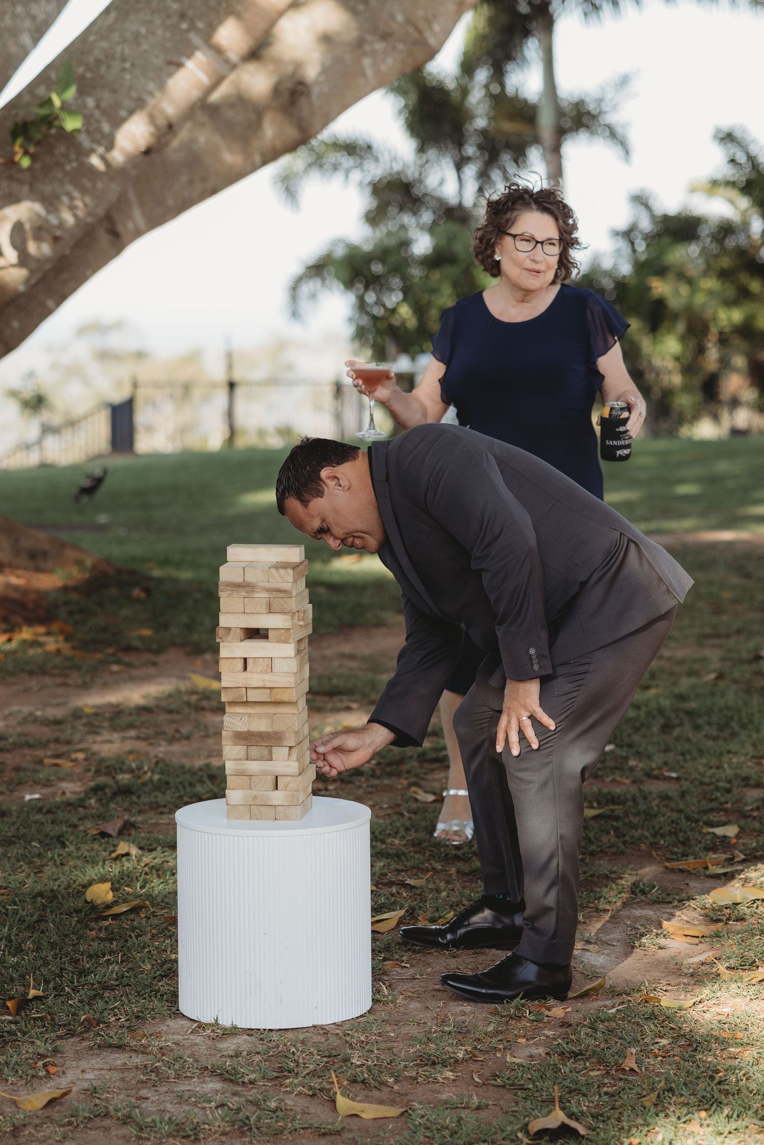 People playing giant Jenga outdoors on a white pedestal during a casual gathering.