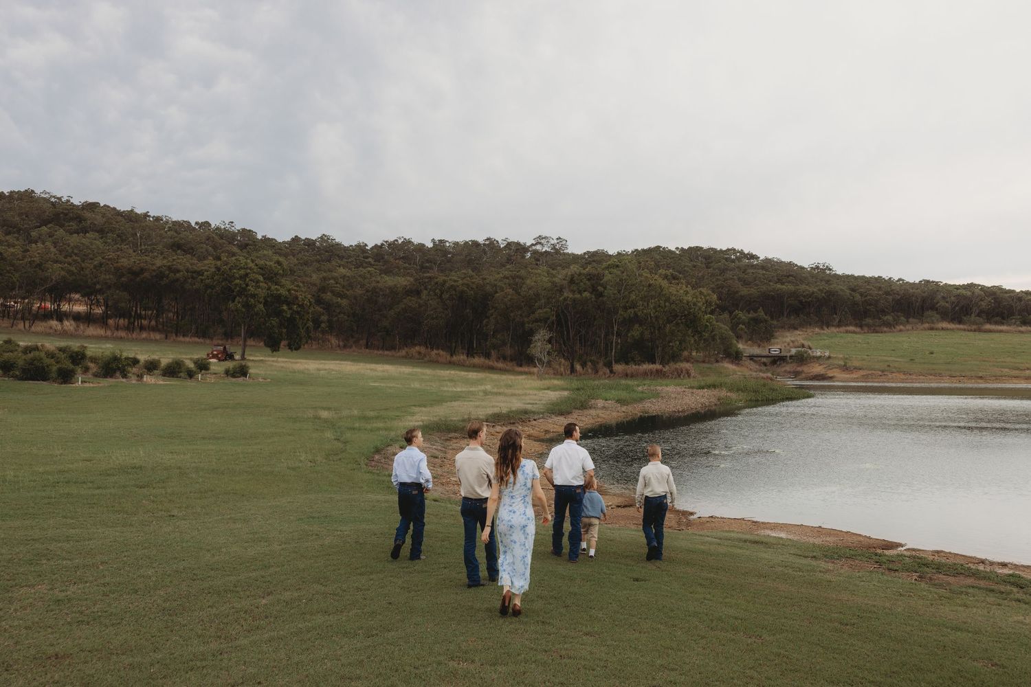 Wedding guests gather on a grassy lawn near a waterfront venue for an outdoor celebration.