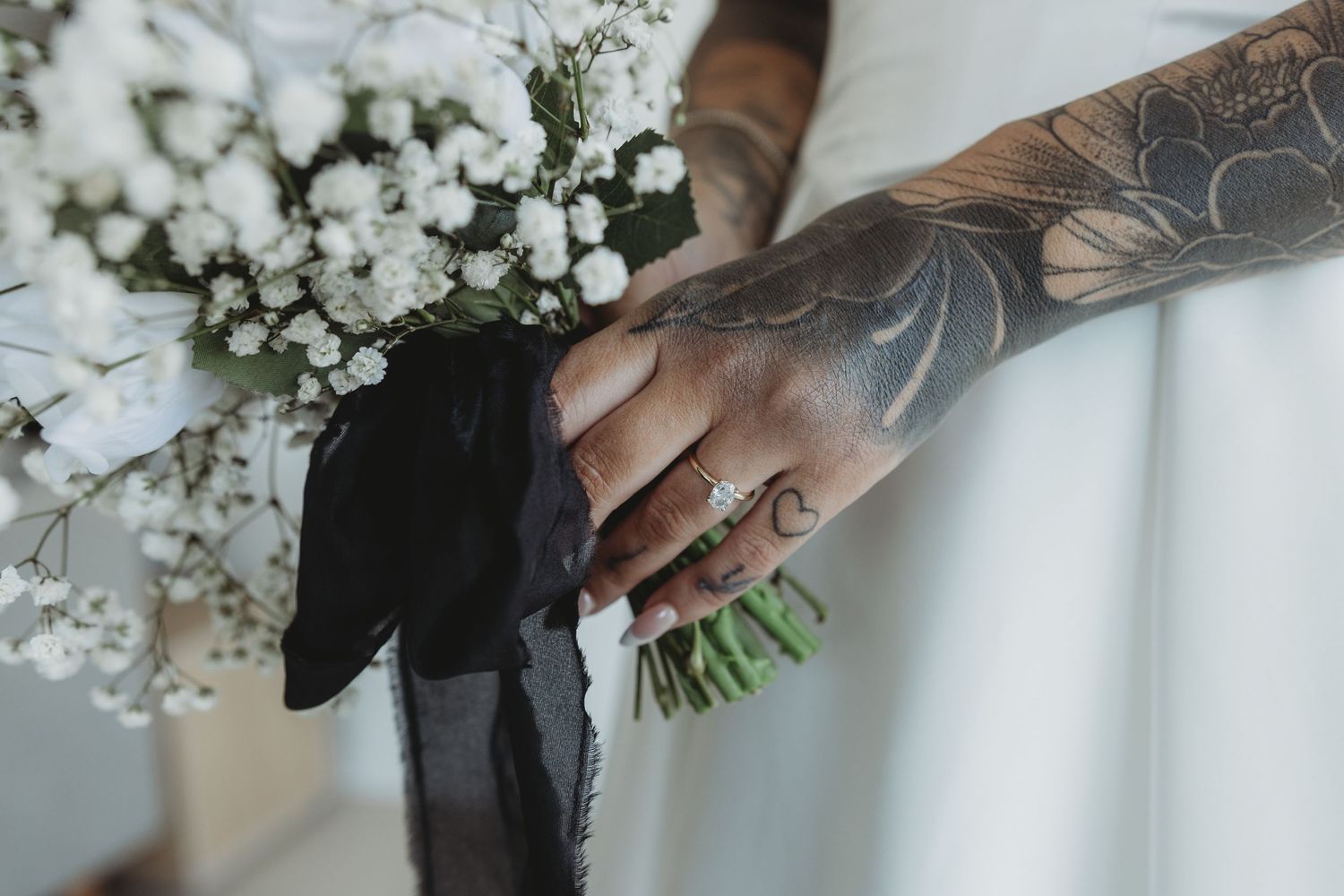 Close-up view of hands holding an elegant white floral wedding bouquet against a light background.