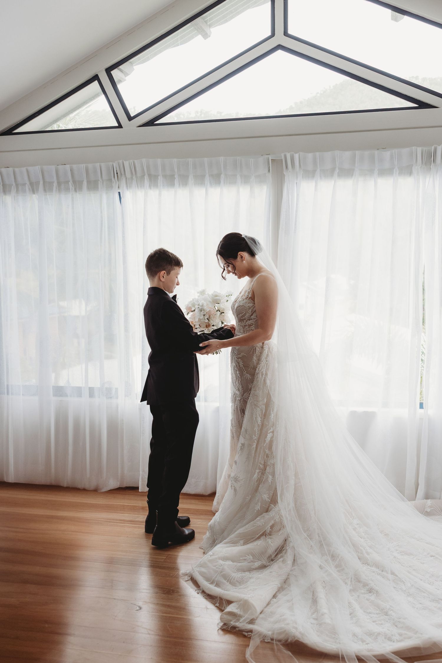 A series of wedding preparation photos showing the final touches being made to a flowing white lace gown in a bright room.