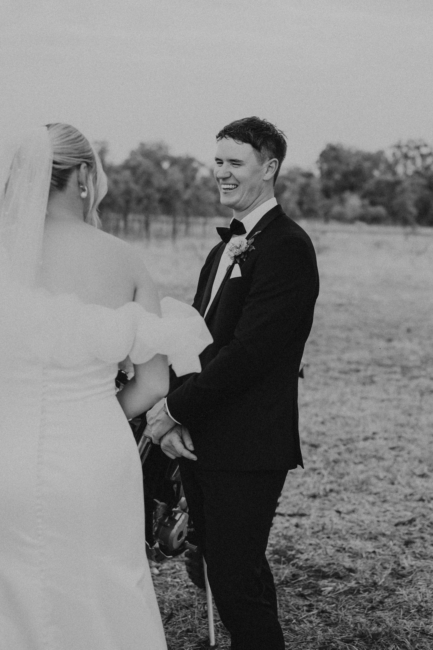 Black and white wedding portrait captured in rustic outdoor field setting.