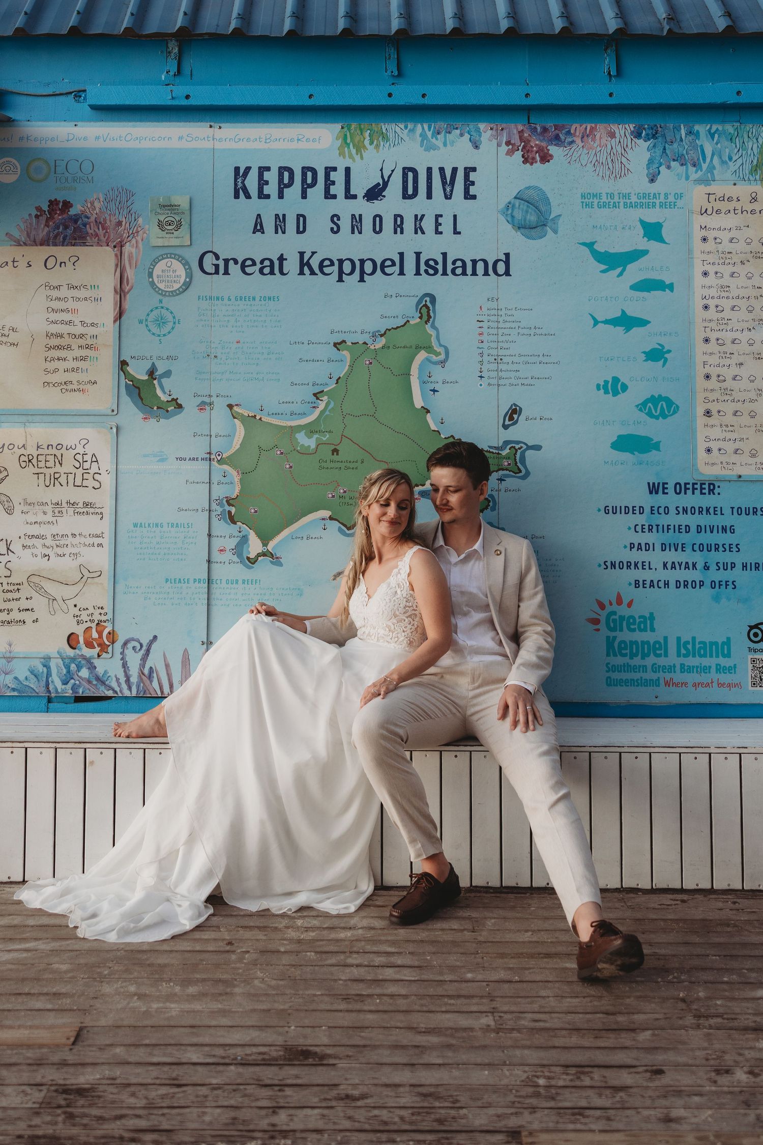 Couple in wedding attire poses against blue wall with map and diving artwork at Keppel Island.