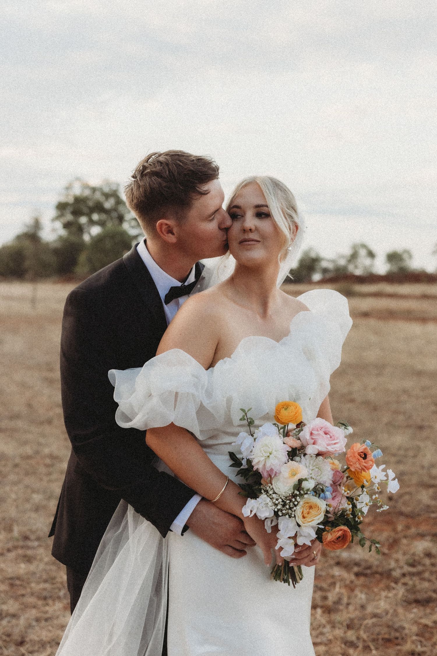 Wedding portraits featuring elegant white dress, colorful bouquet and intimate moments in rustic field.