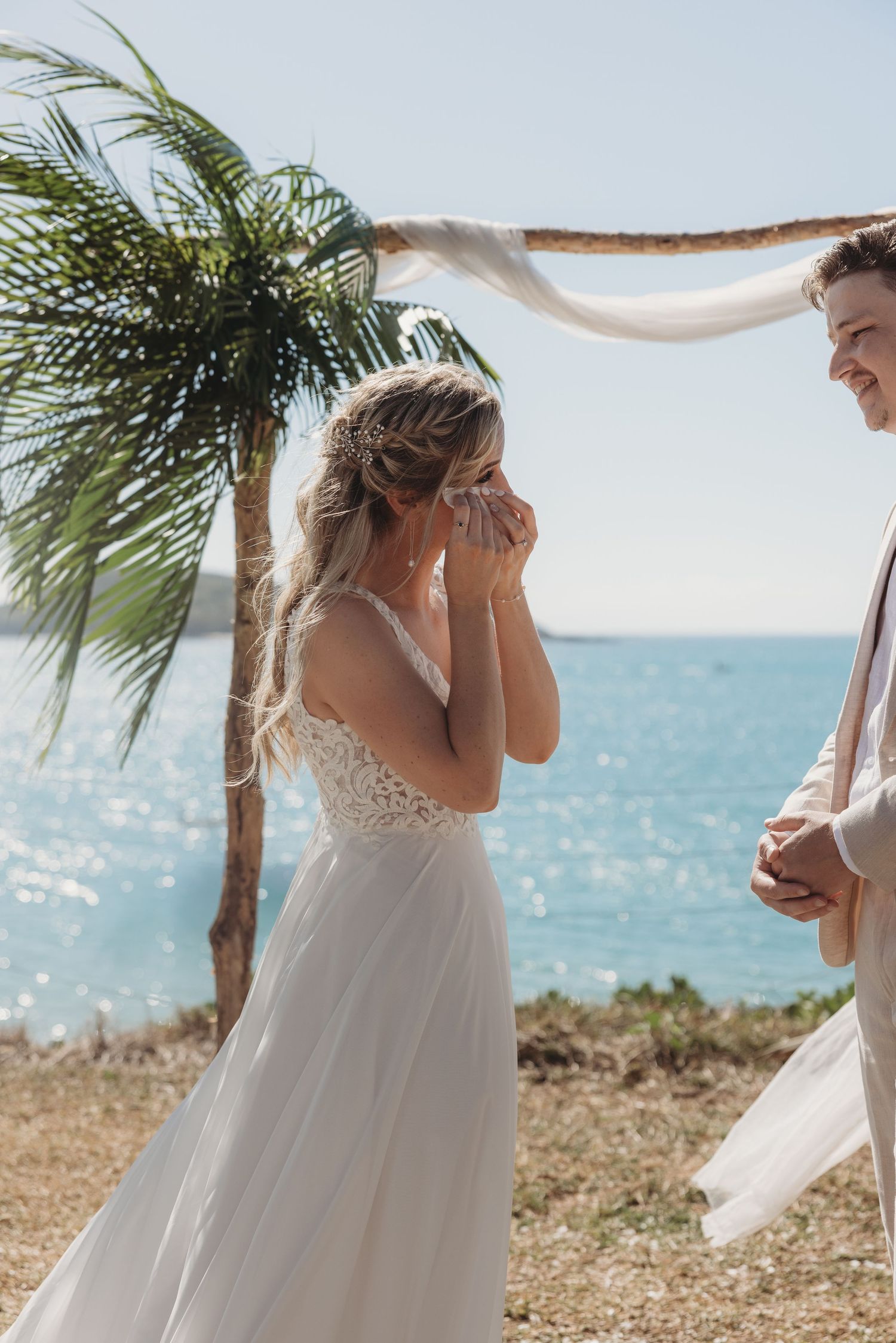 Intimate beach wedding ceremony with white fabric arch and turquoise ocean backdrop.