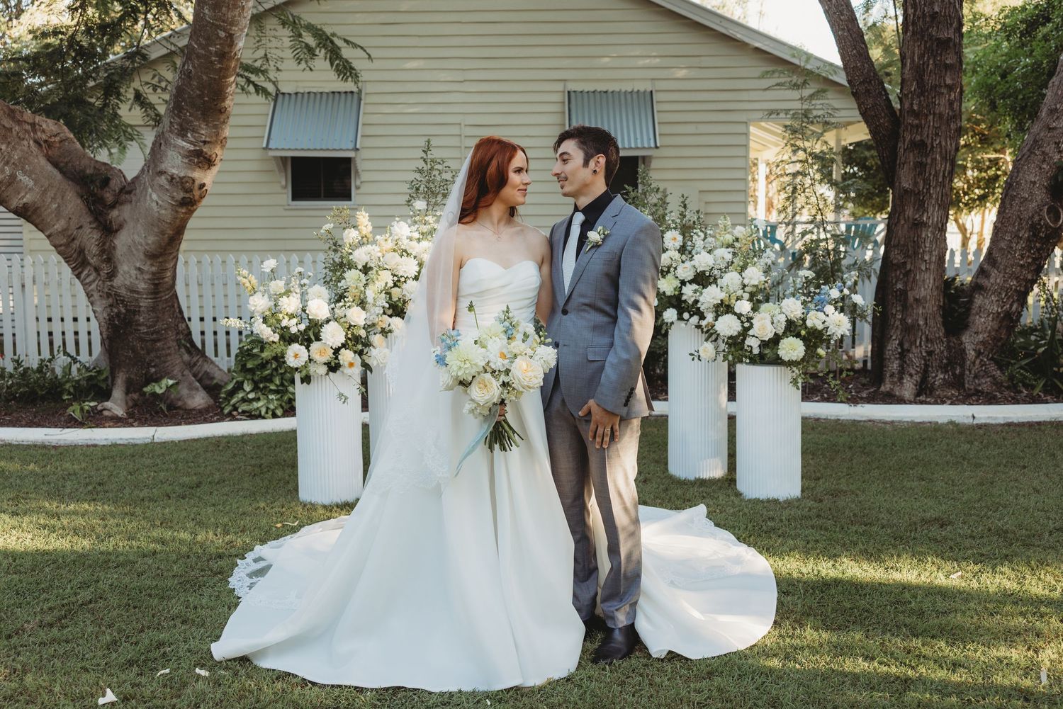 Elegant wedding portrait with couple standing between white floral arrangements outdoors Rockampton wedding