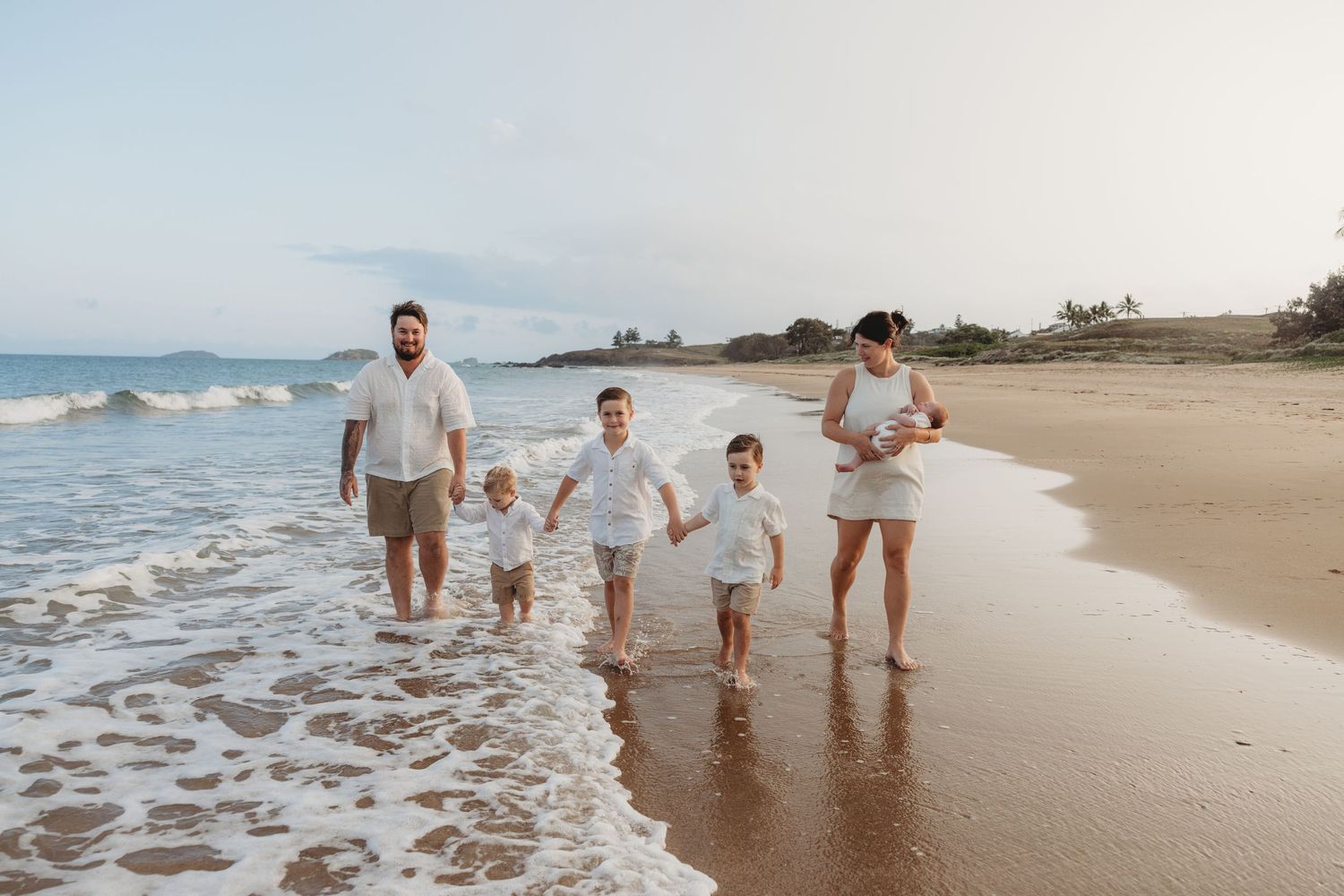 Family walking together along a scenic beach shoreline at sunset with waves crashing nearby.